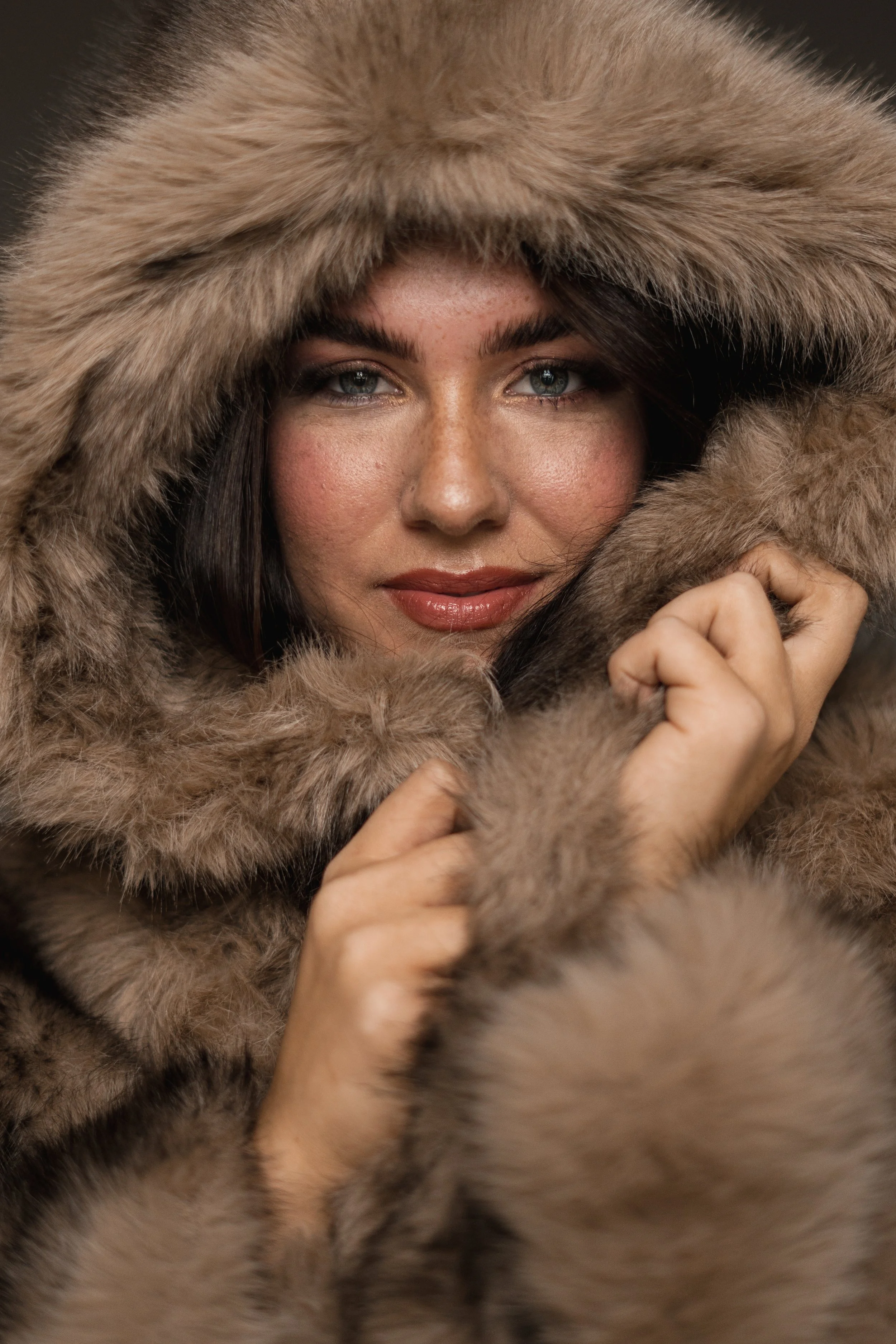 Close-up van een vrouw met blauwe ogen die een bontjas met een capuchon van bont draagt.