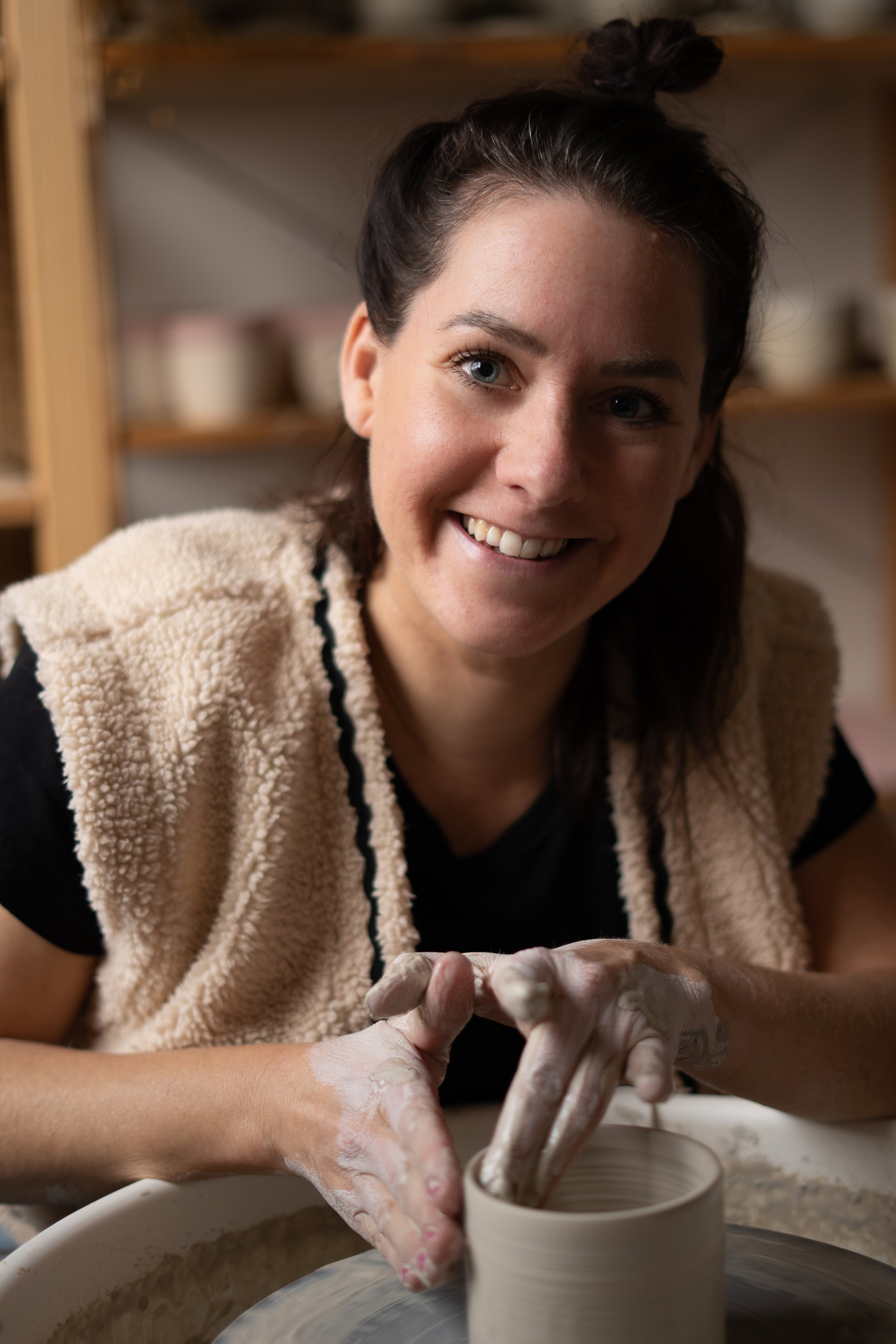Vrouw die keramiek vormt op een draaischijf, glimlachend naar de camera in een atelier.