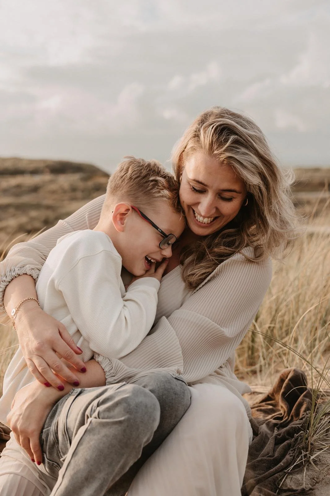 Een vrouw knuffelt een jonge jongen op een veld met gras, beiden lachen en hebben plezier.