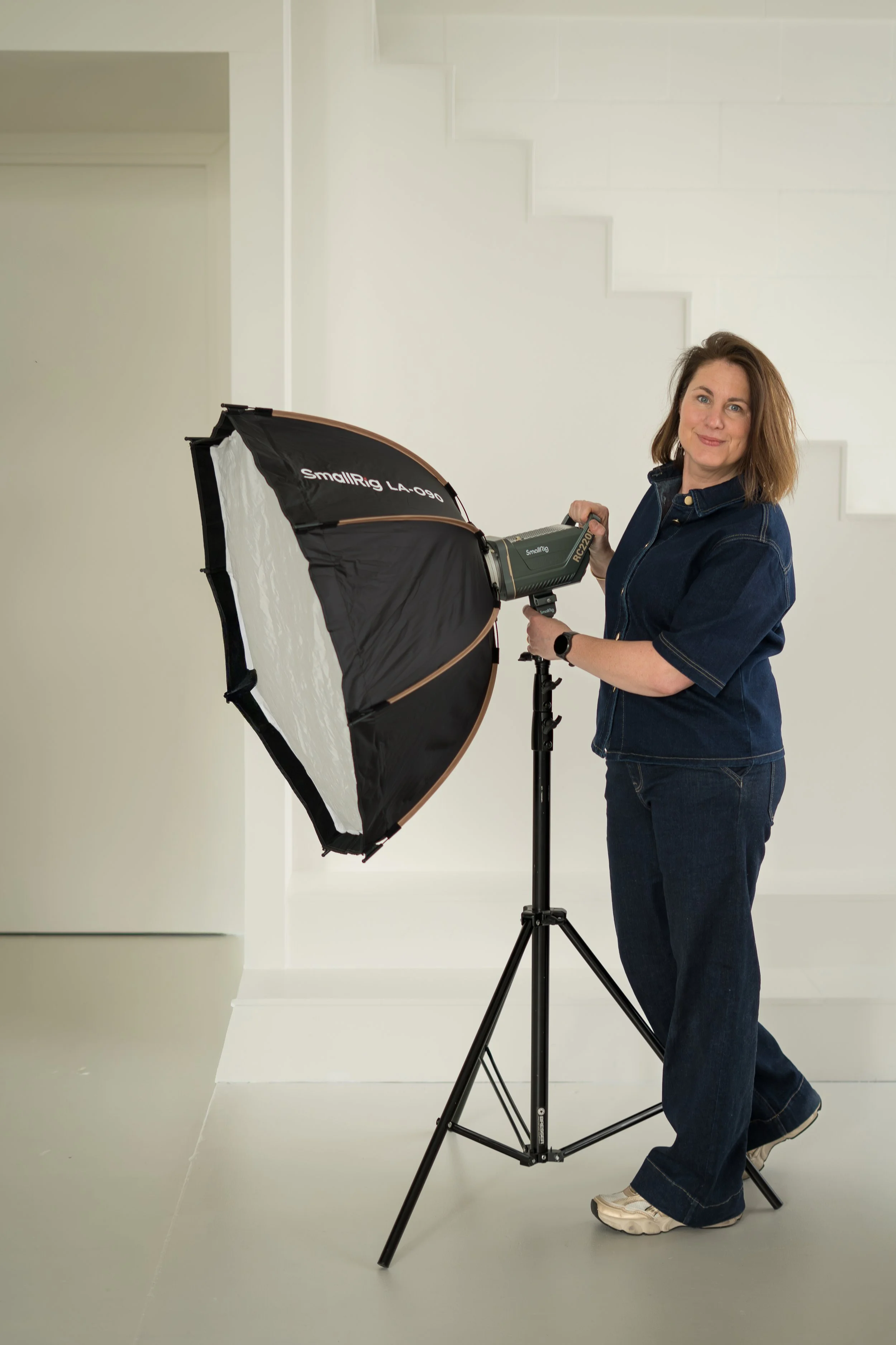 Vrouw houdt een smartphone met een foto galerij omhoog, omgeven door groene bladeren, lachend en in een binnenruimte.