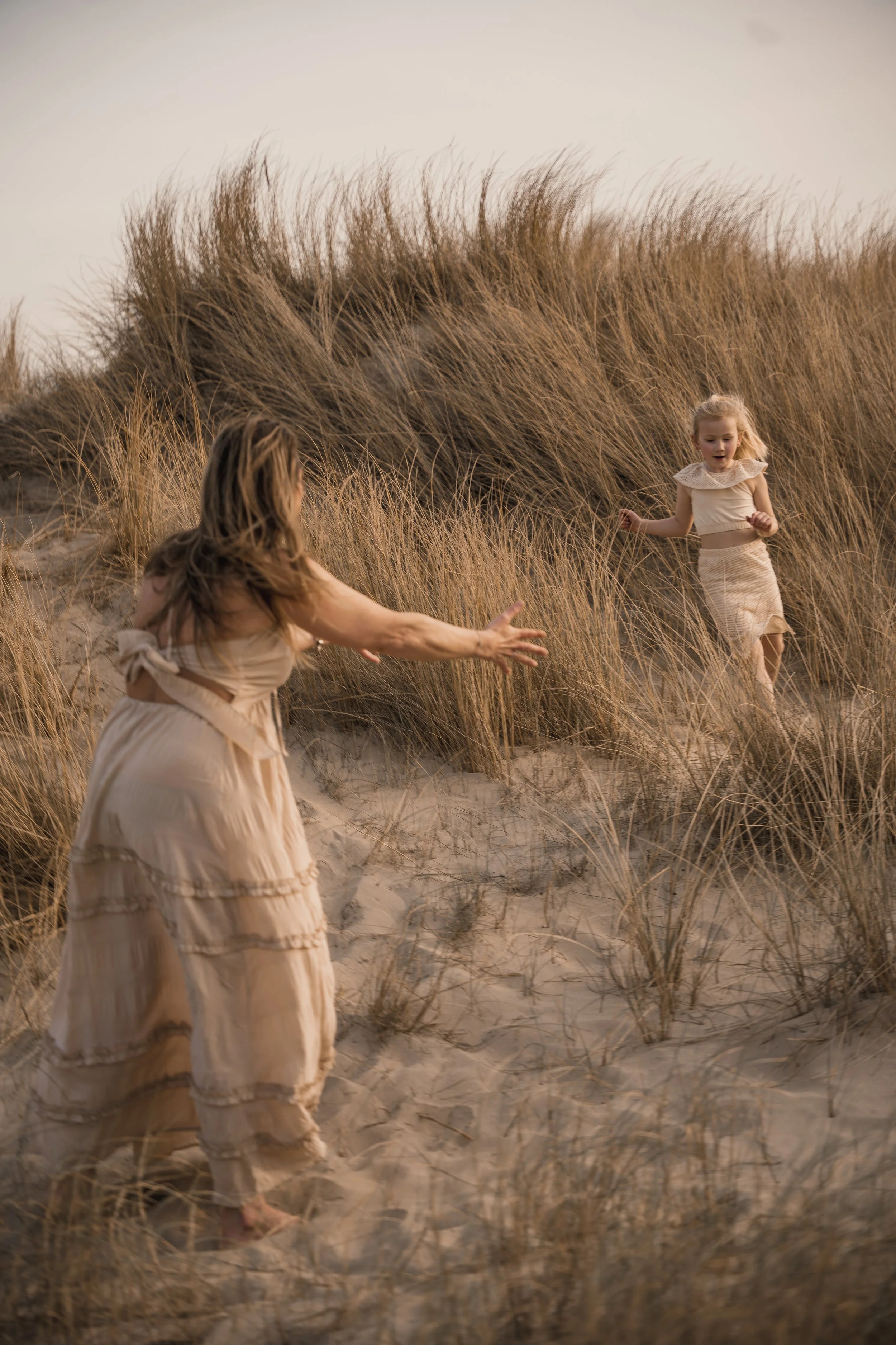 Twee vrouwen die op een zandduin tussen gras spelen, zonsopgang of zonsondergang.