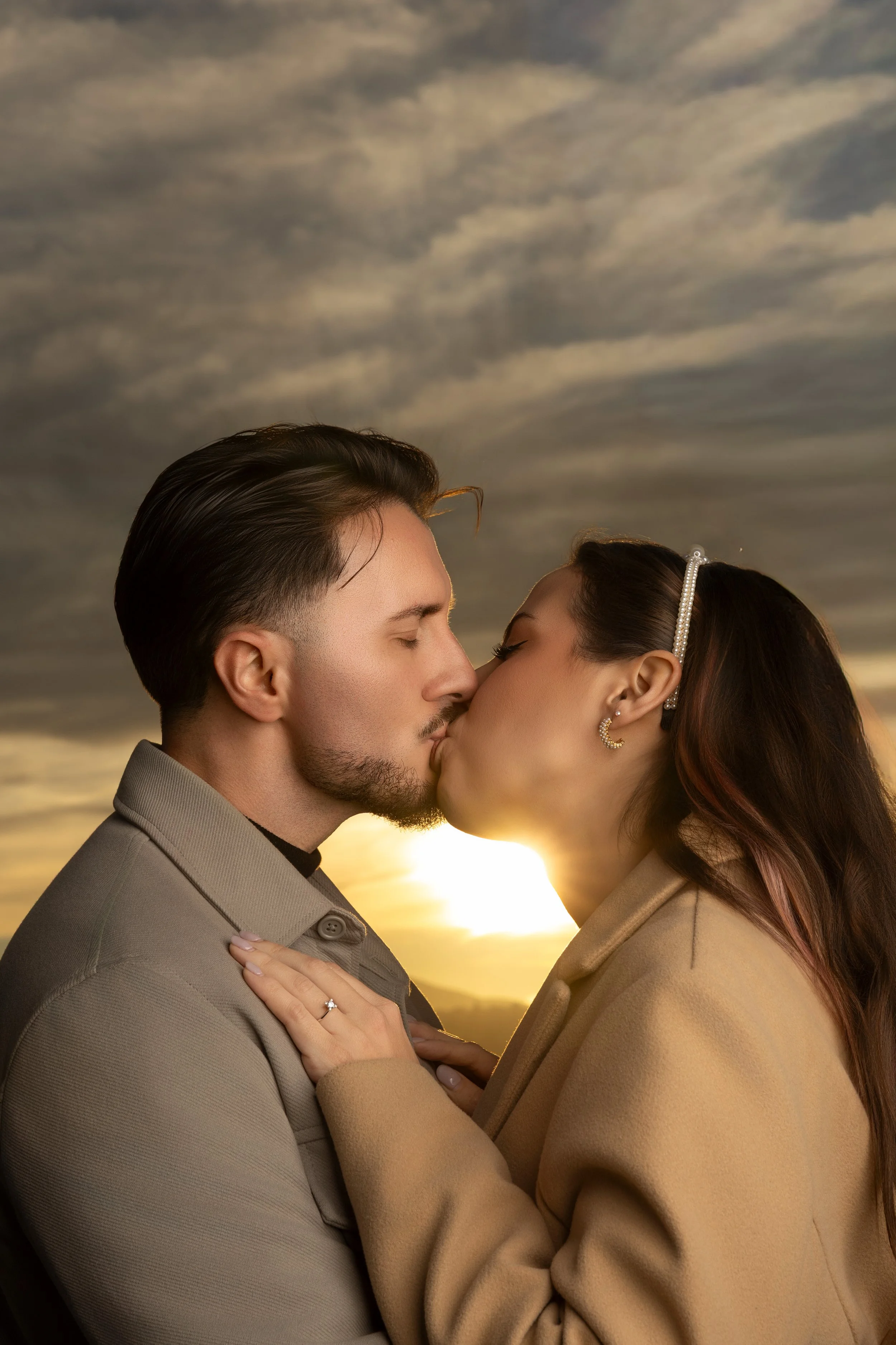 Una pareja besándose al atardecer con un cielo nublado en el fondo.