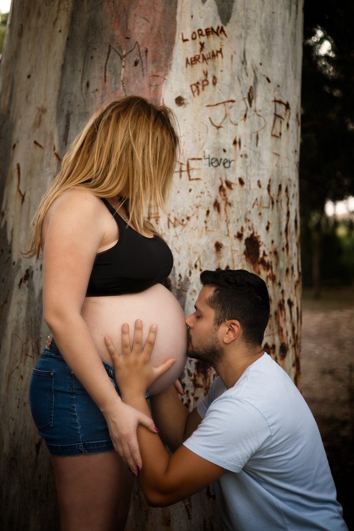 Una mujer embarazada besa a un hombre frente a un árbol con grafiti.