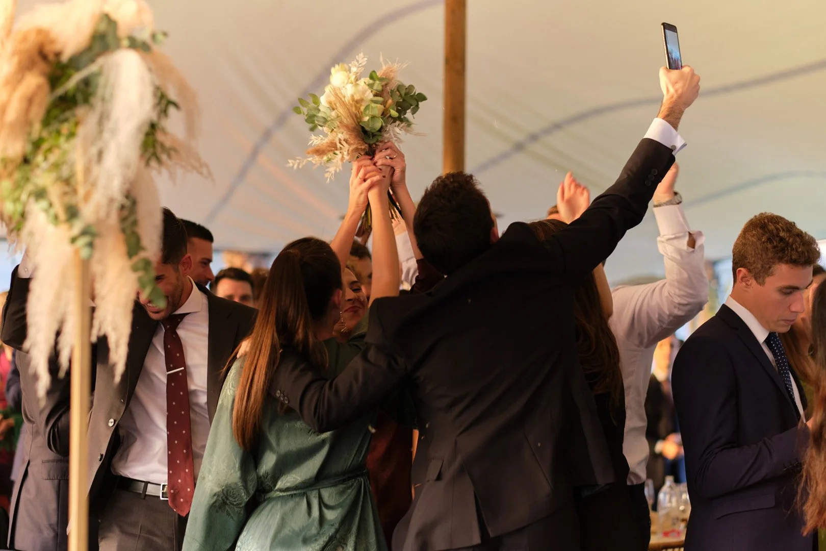 Personas celebrando con un ramo de flores en una fiesta o evento en un espacio cubierto, con iluminación cálida.