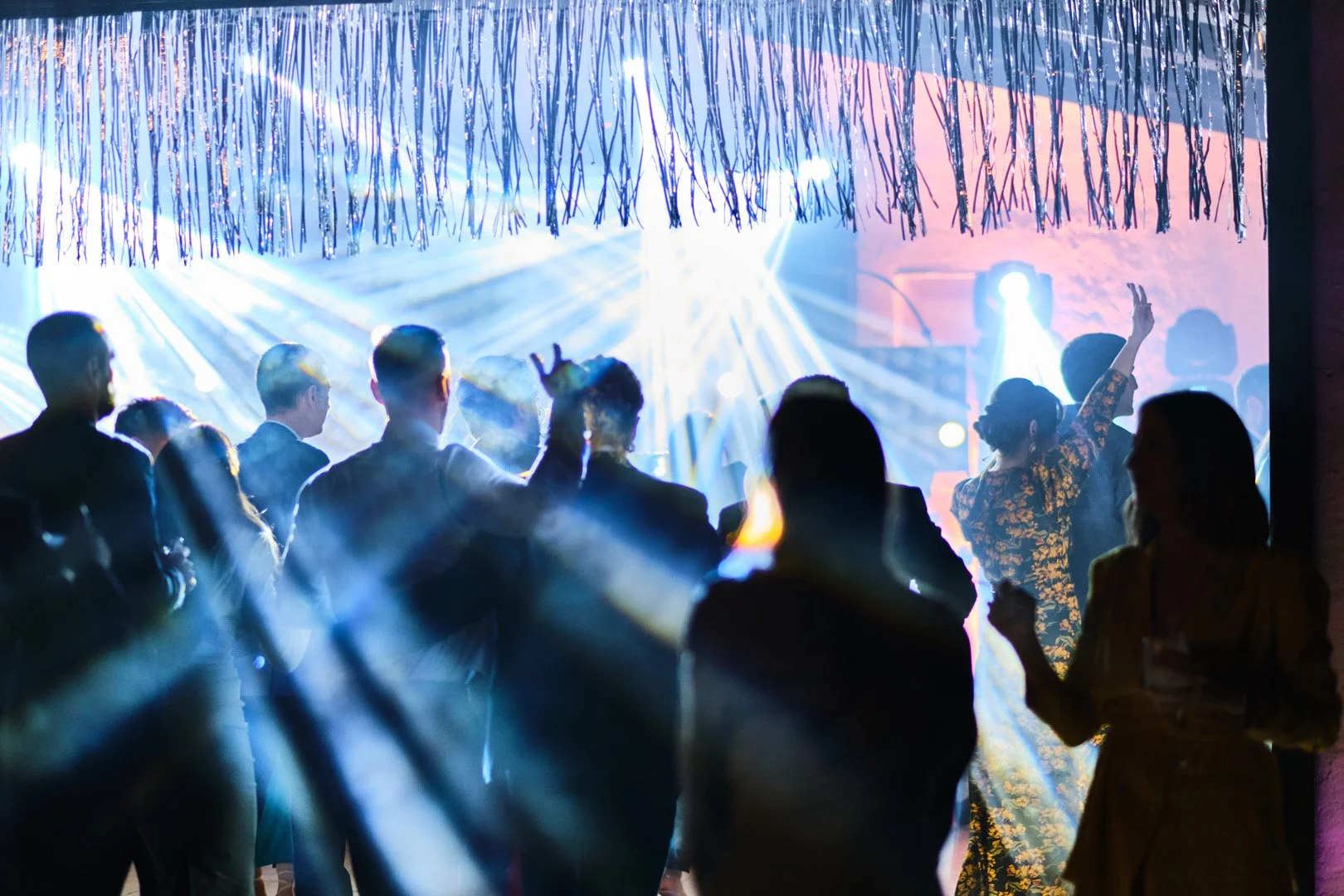 Personas bailando y disfrutando en una fiesta con luces de colores y decoración en el fondo.