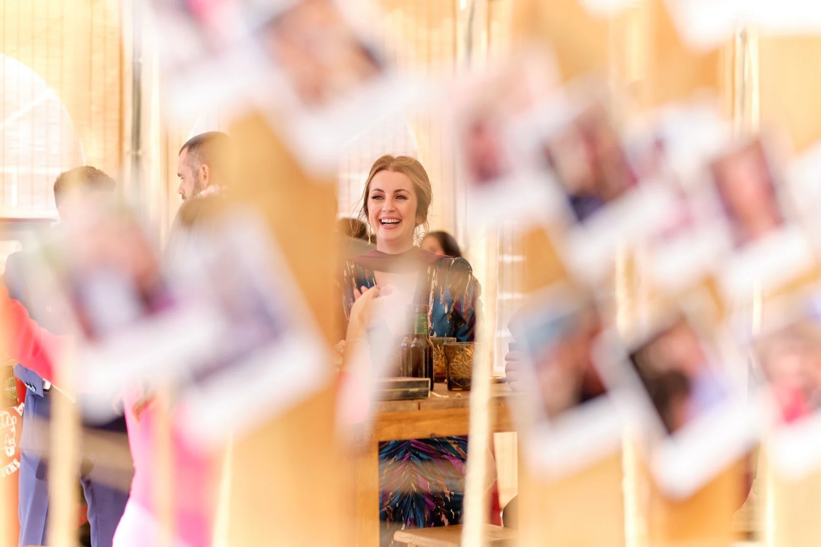 Mujer sonriente en una reunión social, vista a través de una ventana o separación decorativa con fotografías enmarcadas.