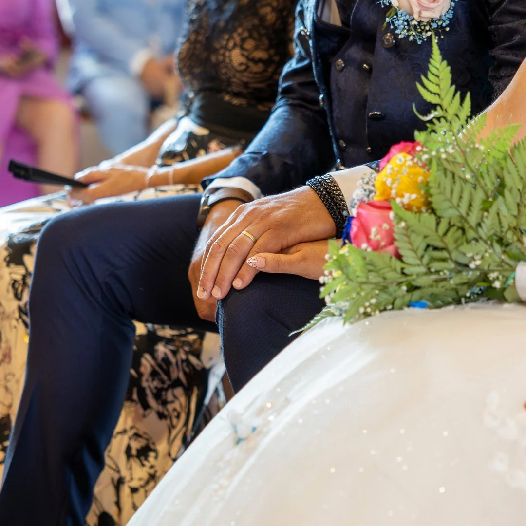 Manos entrelazadas en una ceremonia, con ramo de flores al lado.