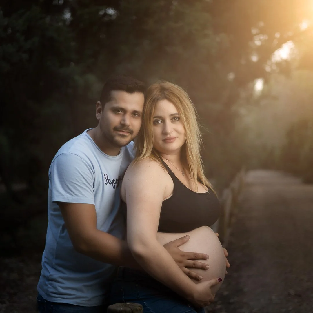 Una pareja, ella embarazada, posa juntos en un camino al aire libre con luz de atardecer.
