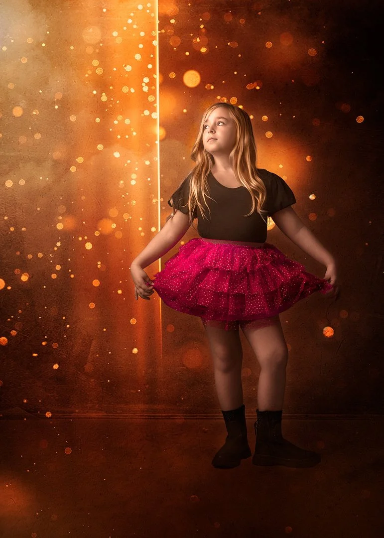Niña con vestido rosa ruffled y camiseta negra, de pie en un fondo dorado con destellos de luz.