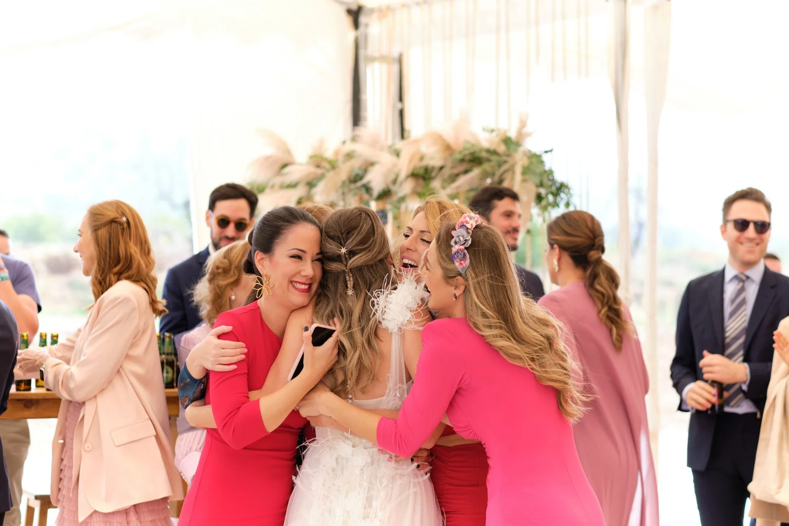 Grupo de personas celebrando en una boda. Mujer vestida de novia siendo abrazada y felicitada por amigos en un ambiente festivo y alegre.