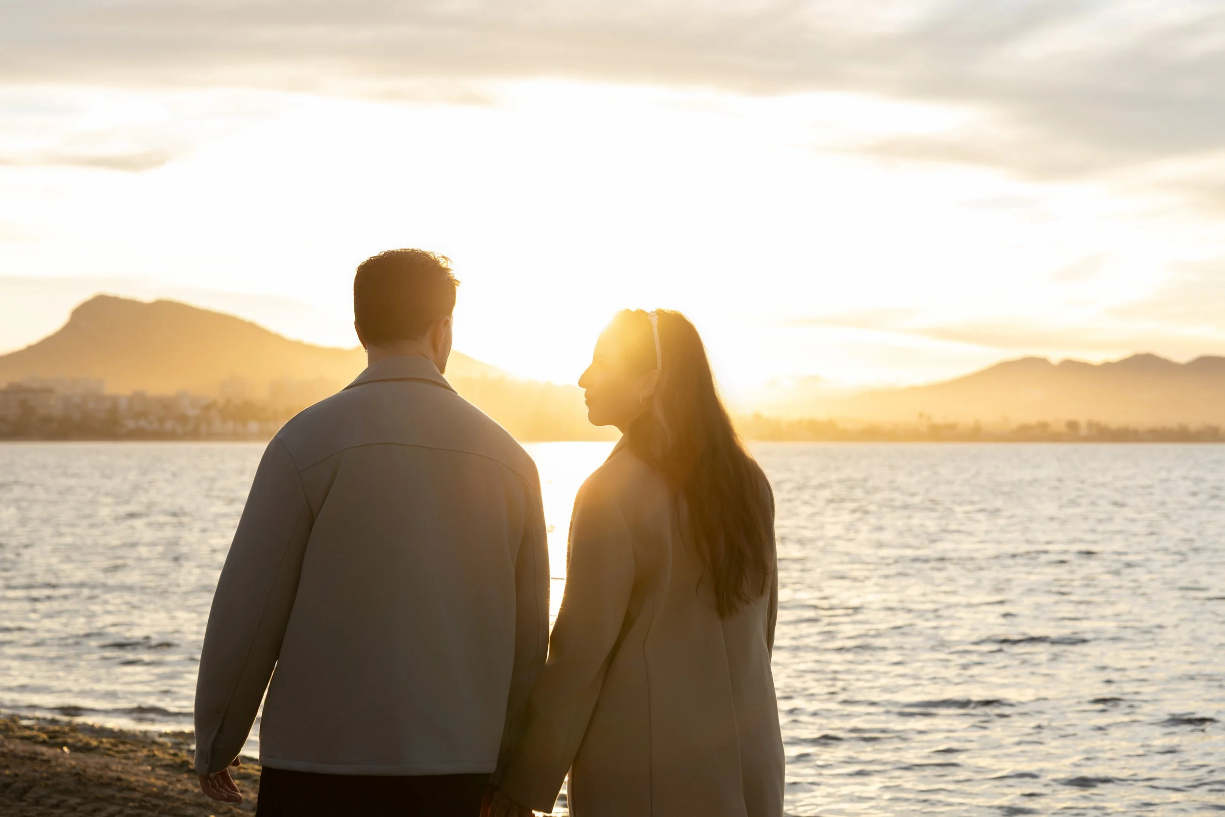 Una pareja caminando junto a un lago durante el atardecer, con montañas al fondo