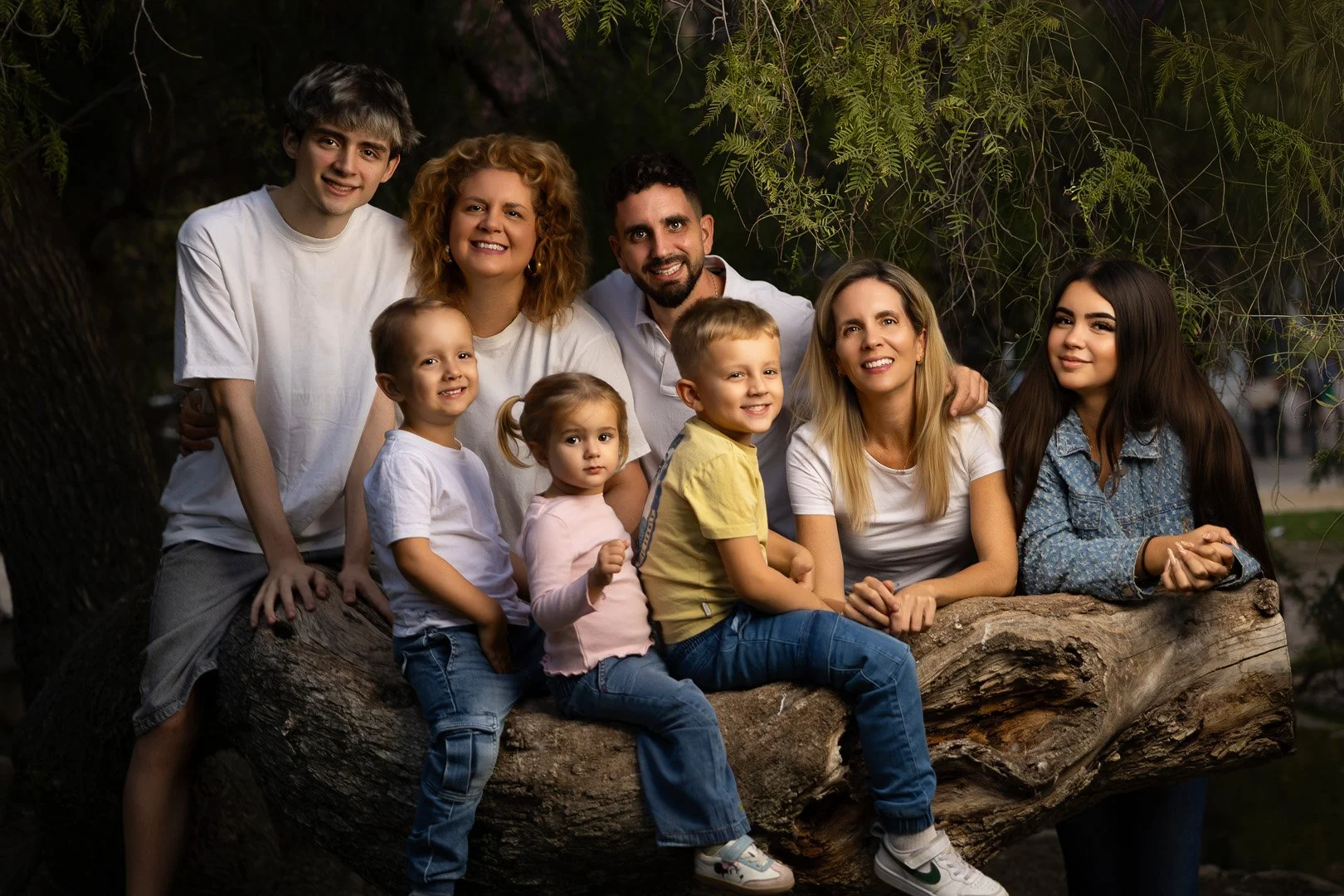 Retrato de una familia de nueve personas posando juntas al aire libre entre árboles, sonriendo y abrazándose.