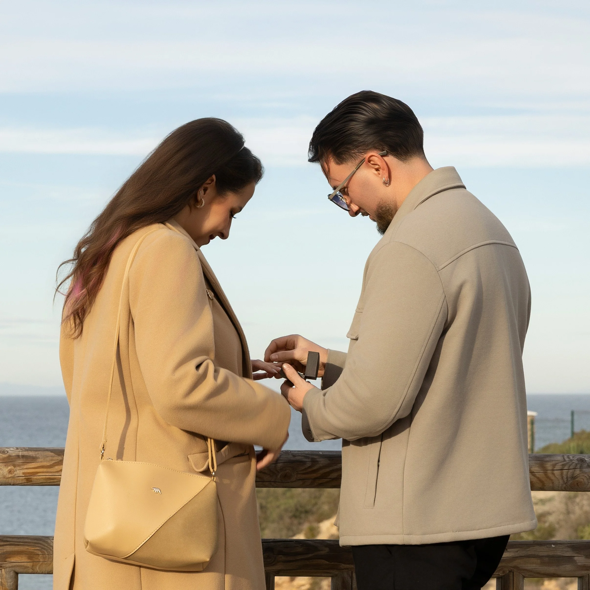 una pareja joven intercambiando un anillo en una ocasión especial con vista al mar en el fondo