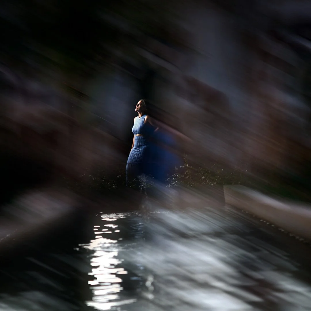 Mujer con vestido azul caminando por el agua en un entorno oscuro con movimiento borroso.
