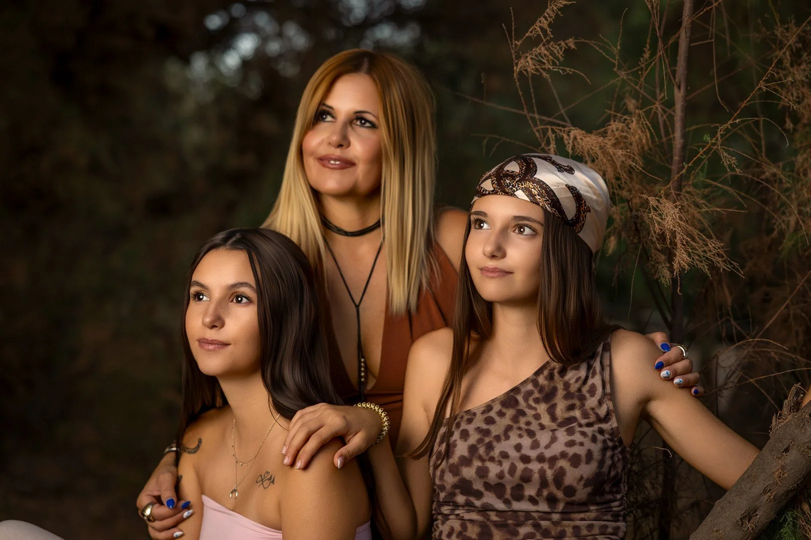 Una mujer adulta acompañada de dos jóvenes, en un entorno natural con árboles y vegetación seca, parecen estar posando para una fotografía.