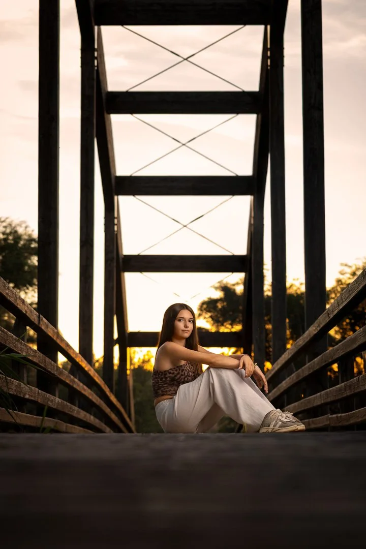 Joven sentada en un puente de madera durante el atardecer