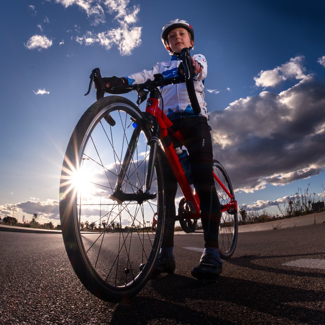 Joven ciclista con casco en bicicleta roja en la calle al atardecer con nubes en el cielo.