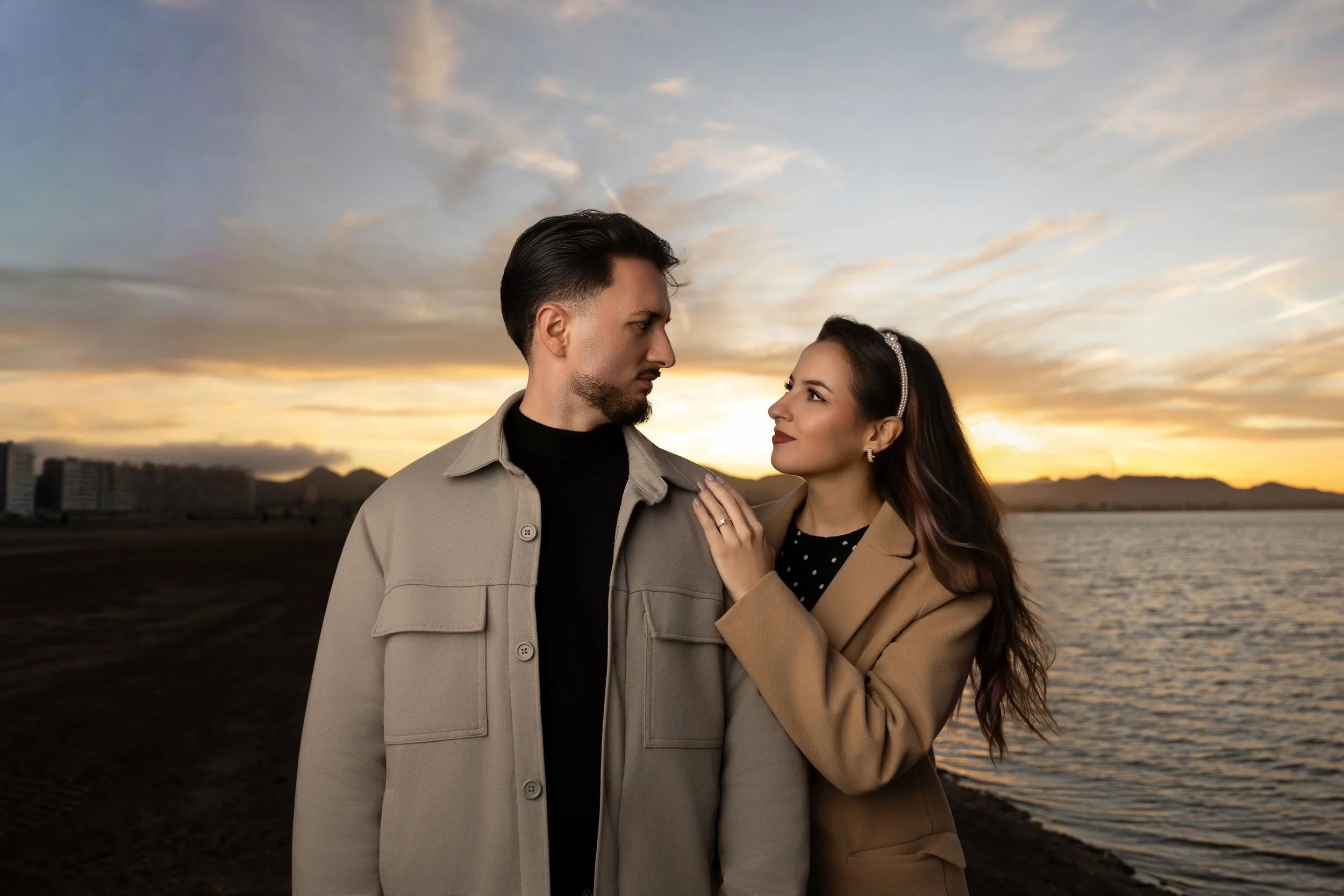 Pareja en la orilla del río durante atardecer, mirándose fijamente.