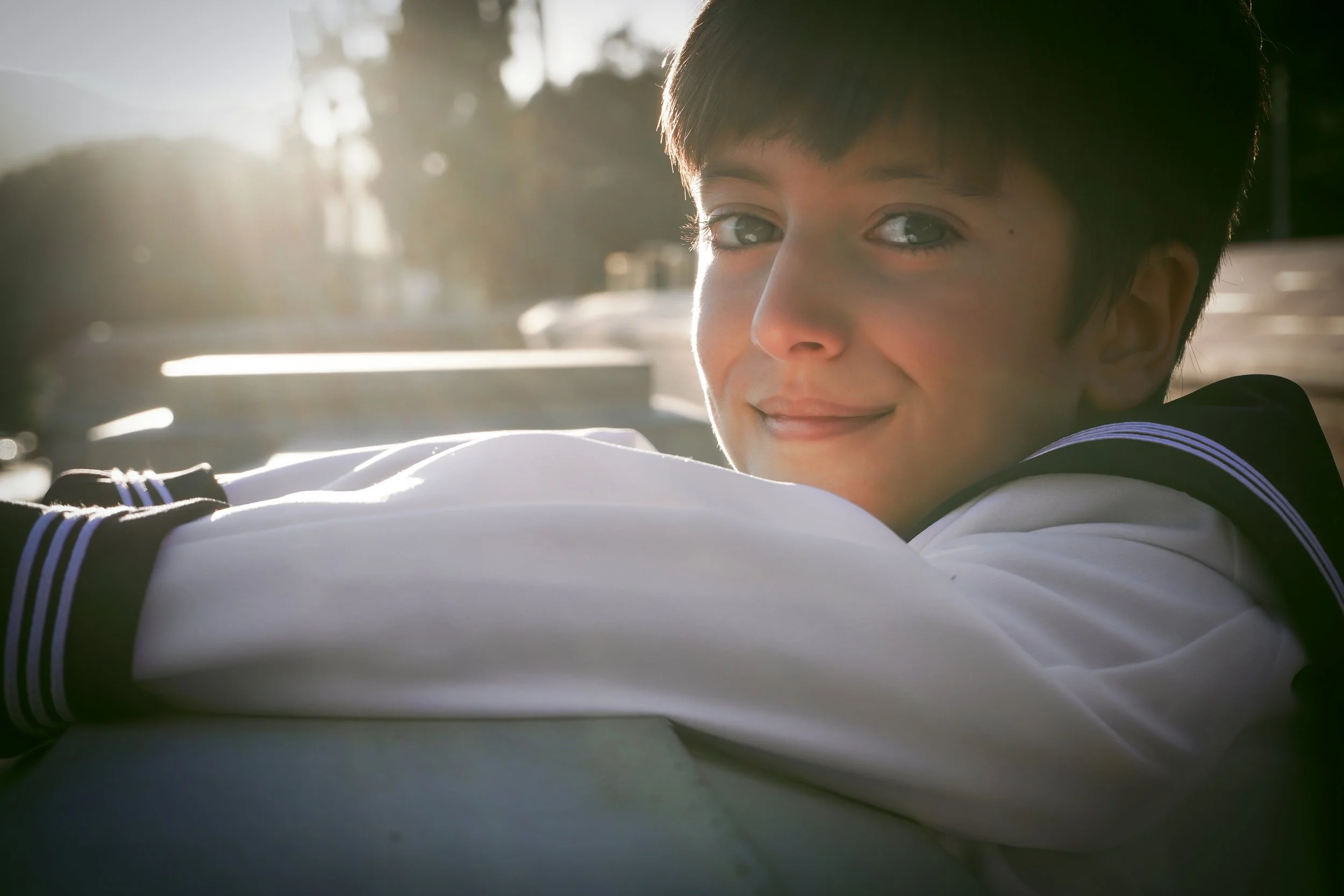 Un niño con traje de comunión de estilo marinero mira hacia la cámara con una expresión dulce, mientras el sol de la tarde ilumina suavemente la escena.