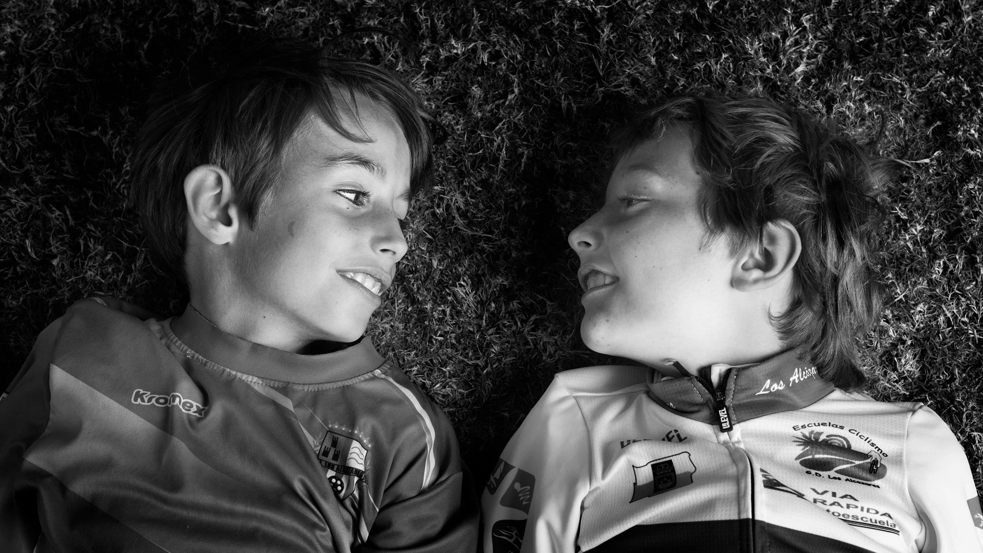 Dos niños con camisetas deportivas mirándose en el suelo en la hierba.