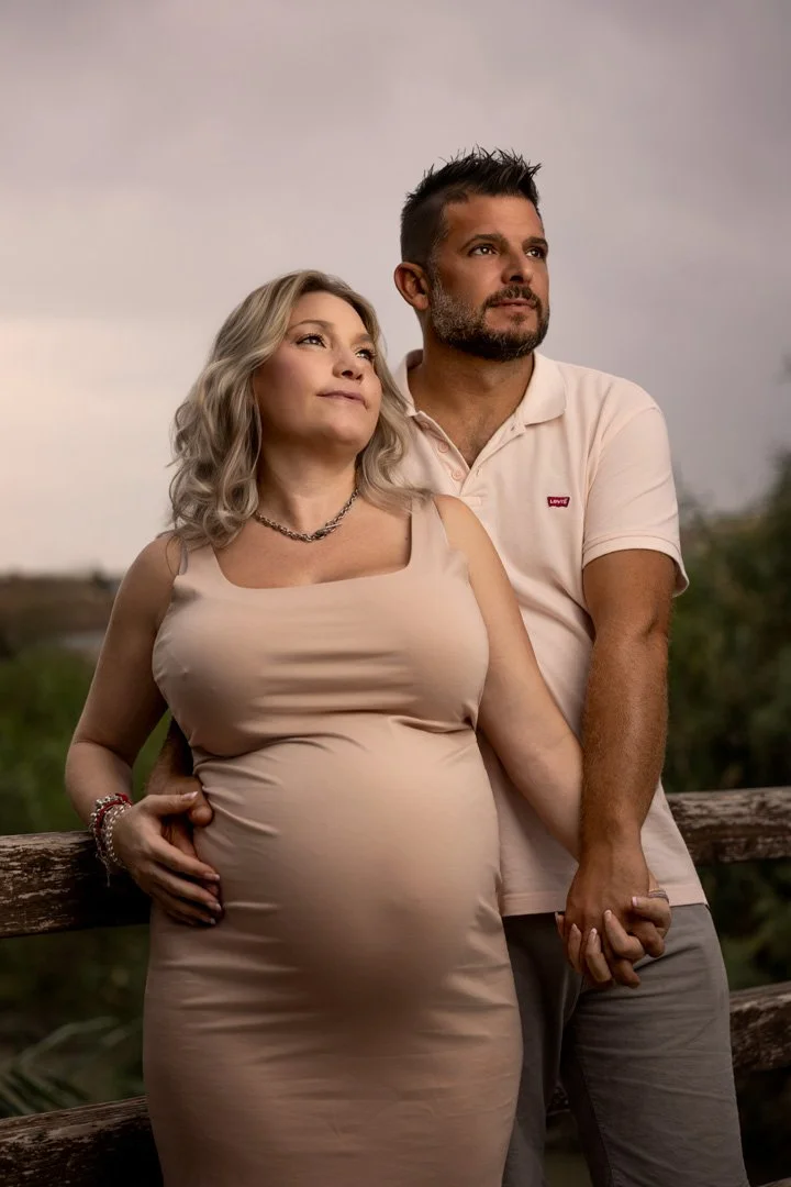 Una pareja posando en un entorno natural, ella embarazada y ambos mirando al horizonte, sosteniéndose de las manos.