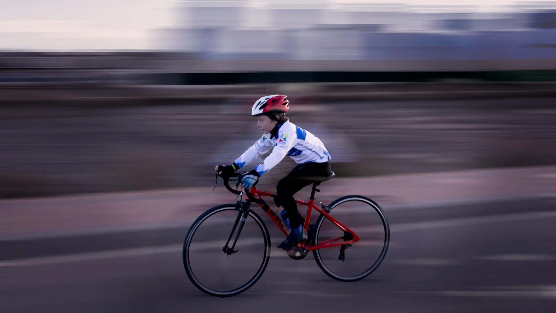 Joven en bicicleta con casco en movimiento rápido en un entorno urbano durante el atardecer.