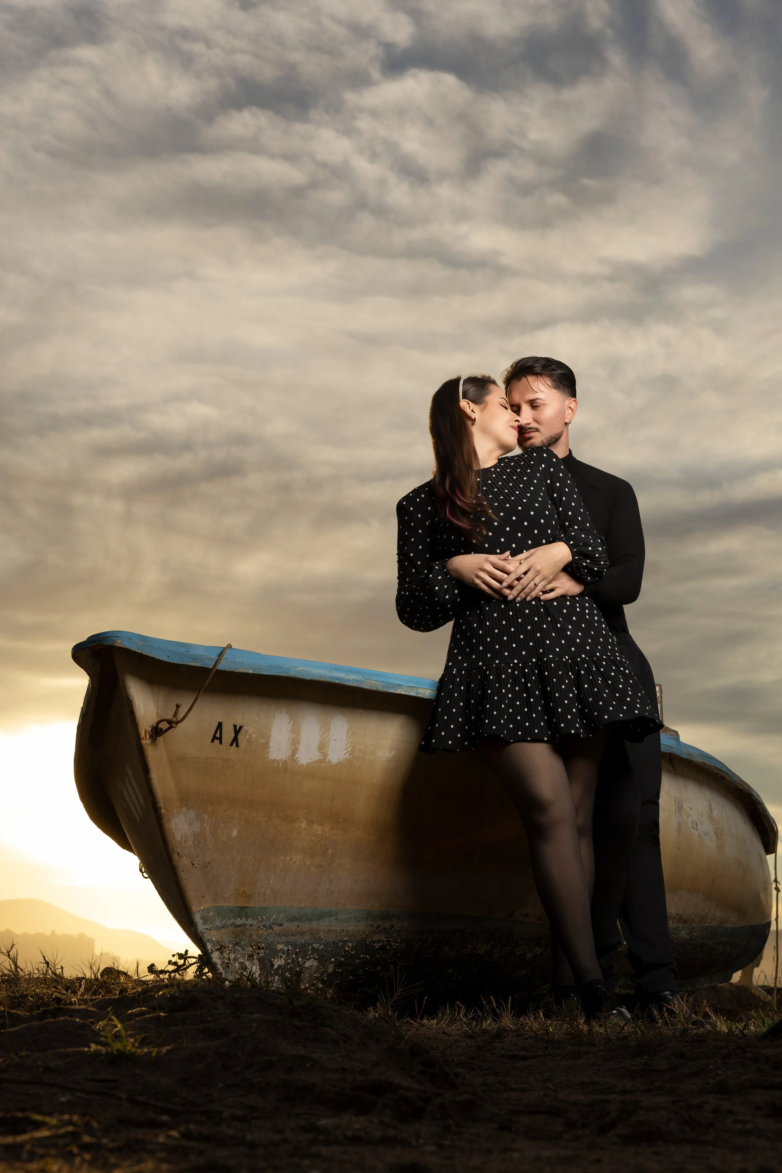 Una pareja abrazada en un muelle de barco al atardecer, con cielo nublado y un fondo natural.