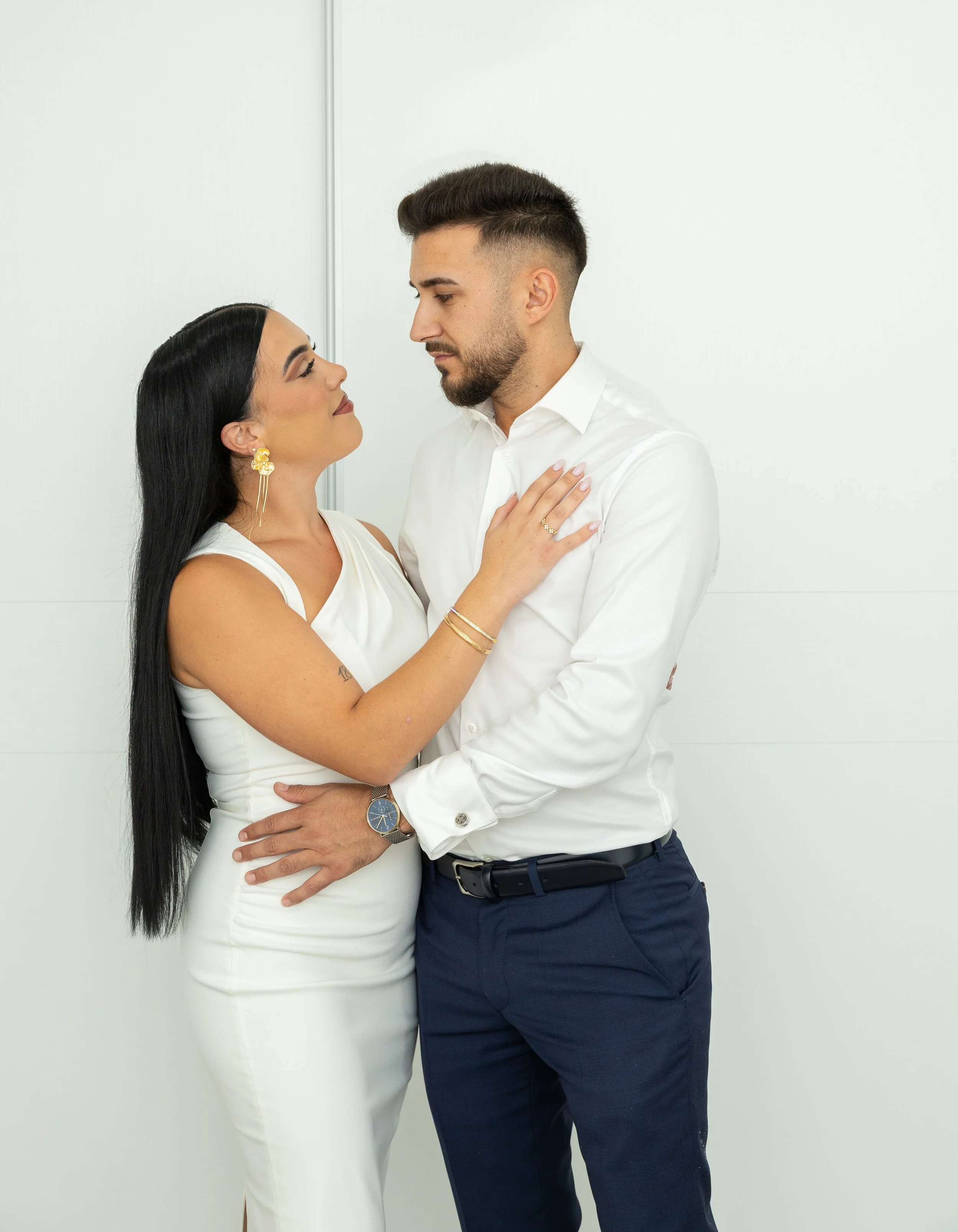 Una pareja mirándose cara a cara, con la mujer tocando el pecho del hombre y el hombre sosteniendo a la mujer por la cintura, en un fondo blanco.