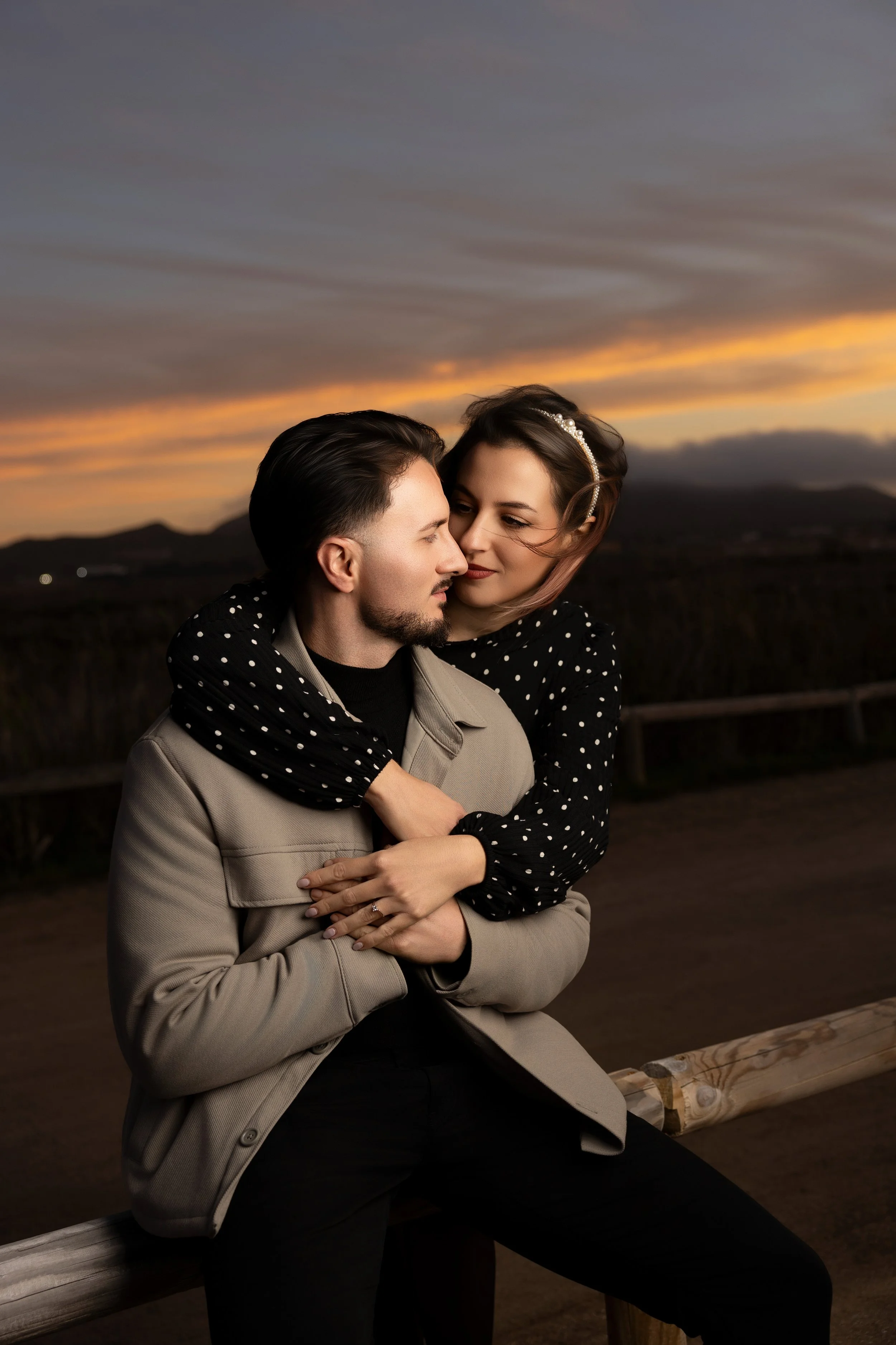 Una pareja en un parque al atardecer, ella le abraza por detrás y ambos se miran con cariño.