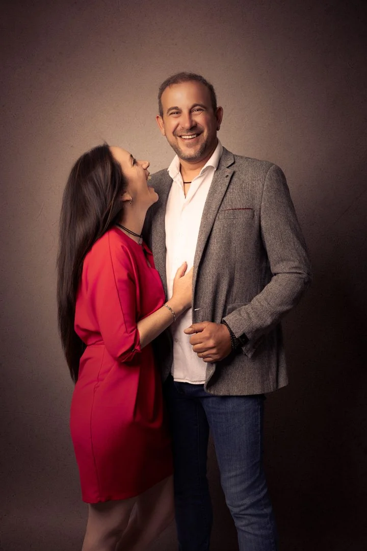 Una mujer y un hombresonriendo y riendo juntos, con la mujer tocando el pecho del hombre, en un fondo oscuro.