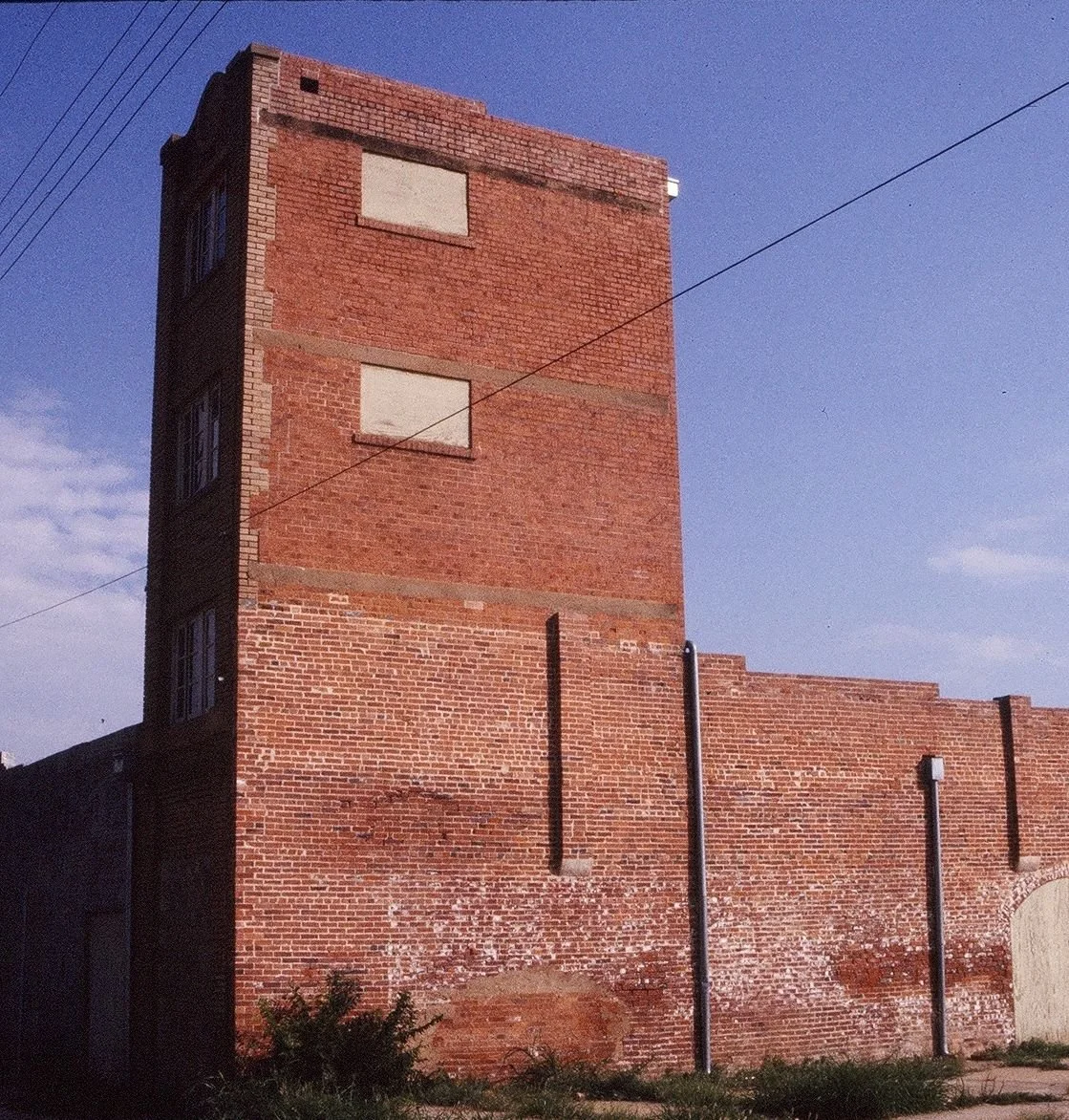 Old red brick building with boarded-up windows and weathered brick wall, under a clear blue sky.