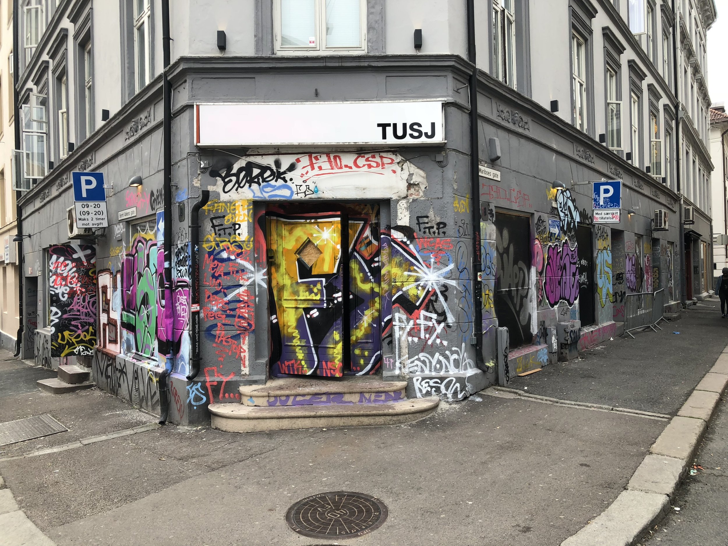 Corner building with graffiti-covered walls and windows, street signs, and a parking meter.