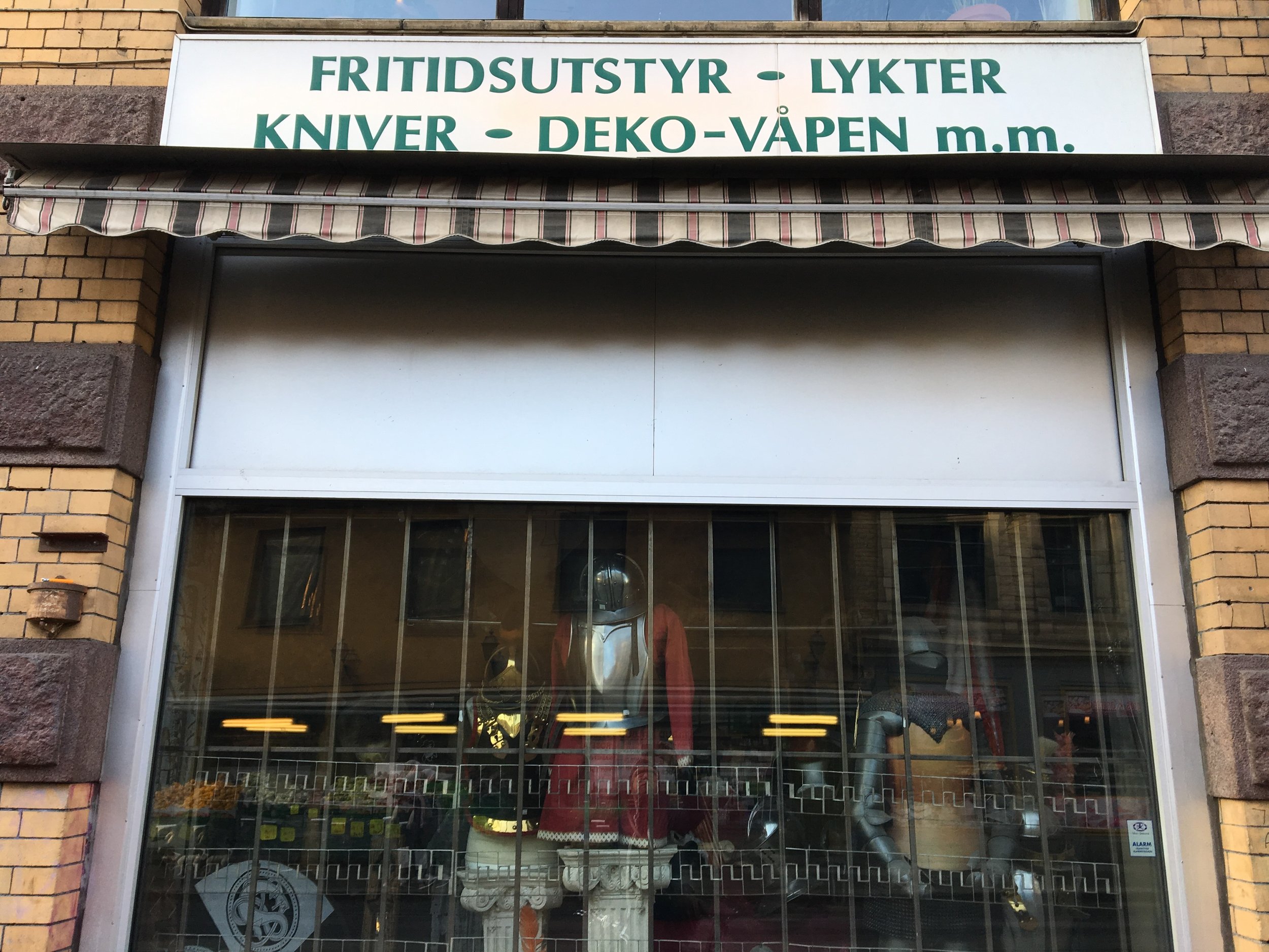 Storefront with a sign in Swedish above a glass window display, featuring mannequins dressed in clothing inside the store.