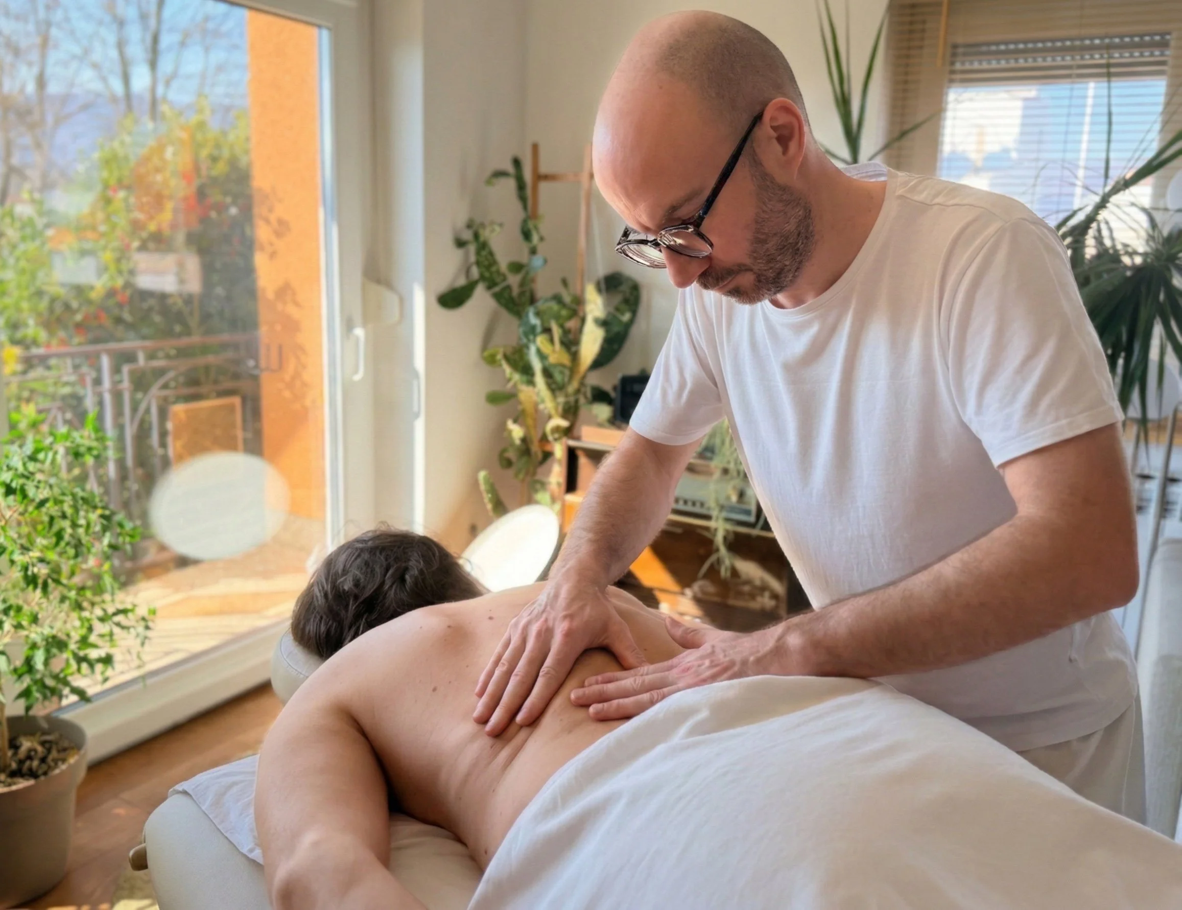Muškarac prima masažu leđa u dobro osvijetljenoj prostoriji punoj biljaka.