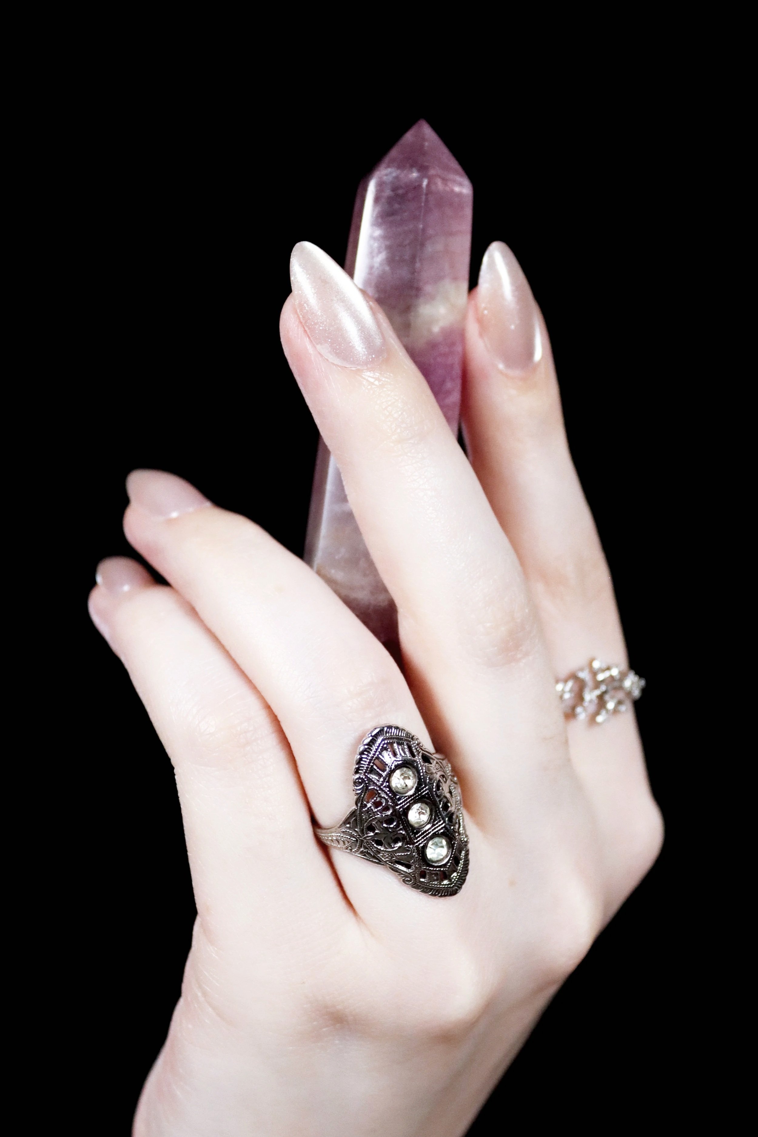 A hand with rings holding a polished purple fluorite tower against a black background.