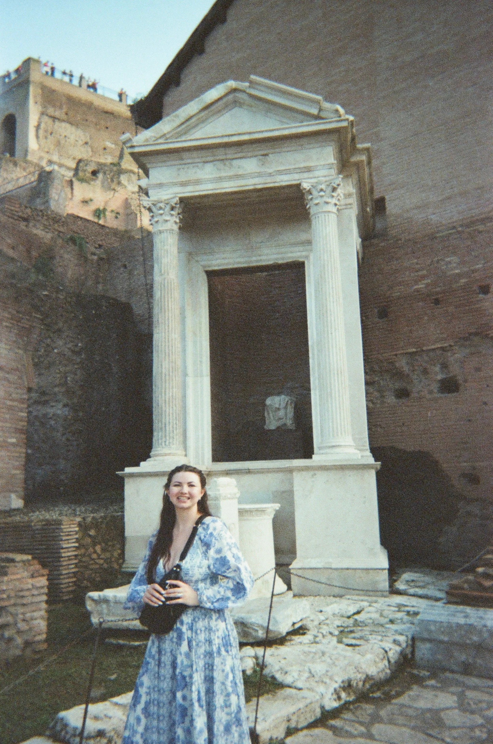 A young woman in a blue and white patterned dress standing in front of an ancient Roman ruin in Rome.