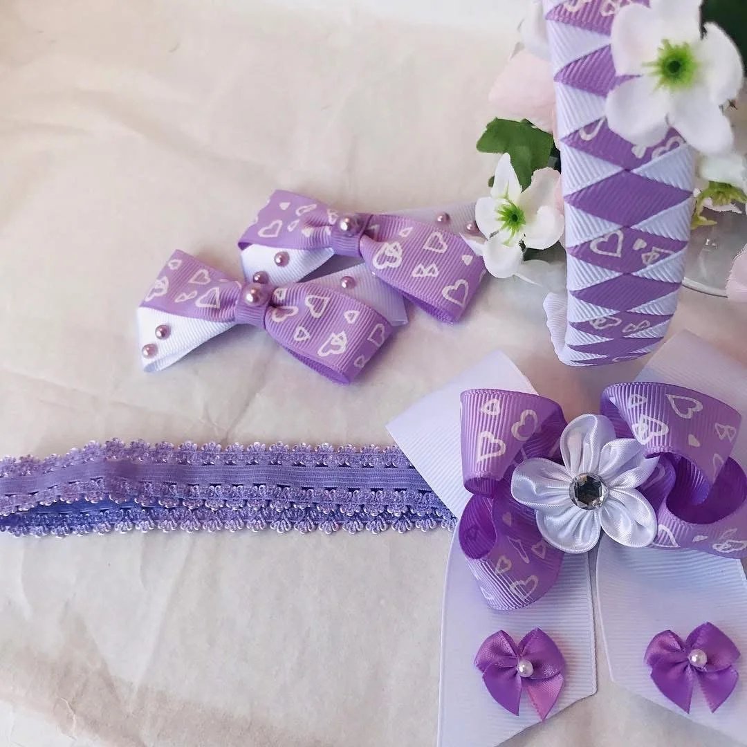 Purple and white hair accessories with bows, ribbon flowers, and decorative patterns, arranged with some white flowers.