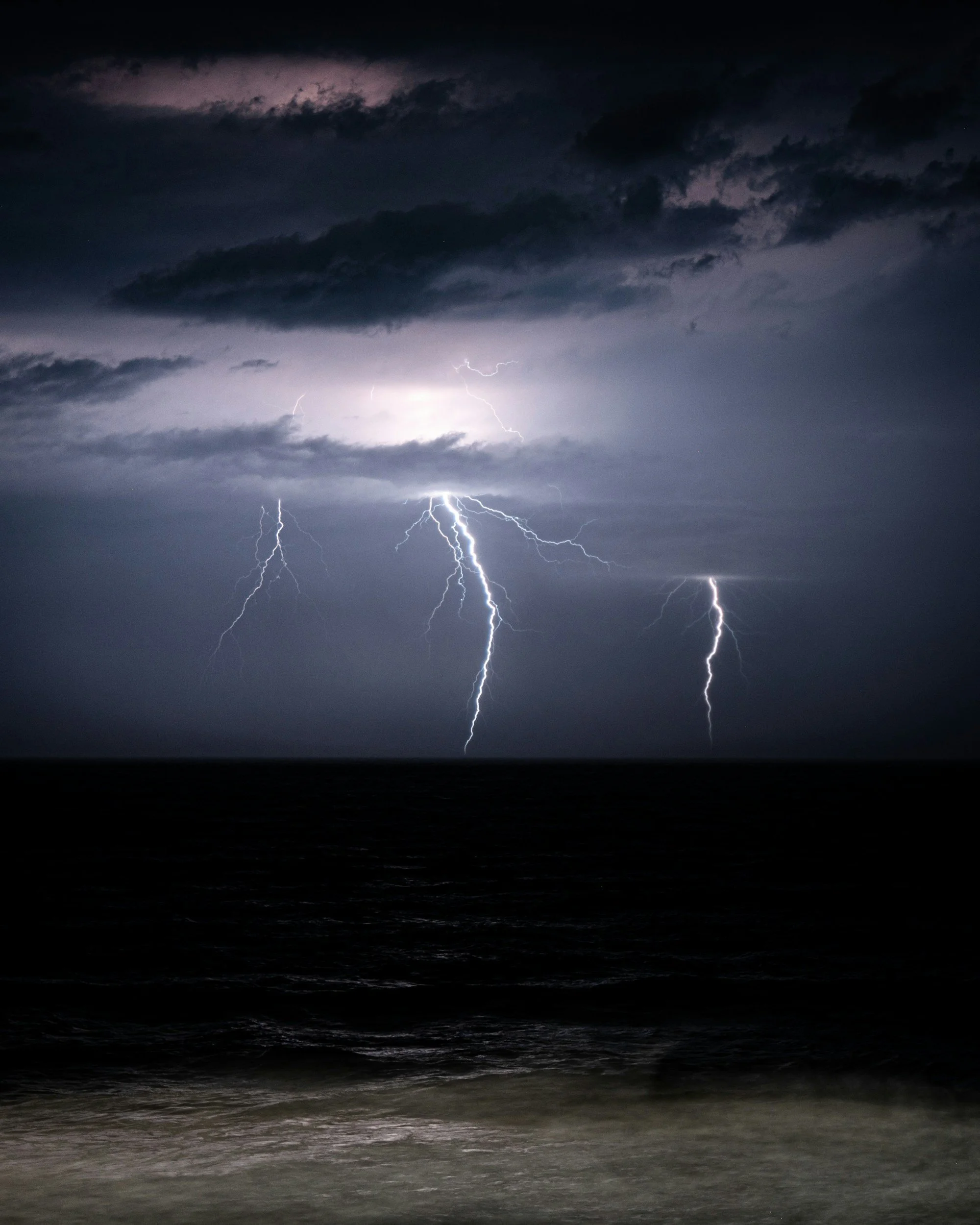 Lightning storm over the ocean at night with dark clouds in the sky.