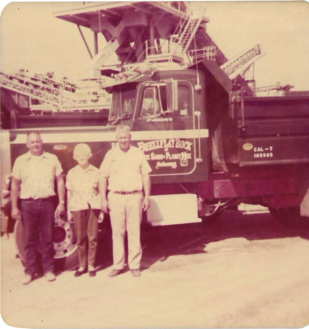 A vintage black-and-white photo showcasing three men standing in front of a large firefighting truck with a ladder on top. The men are dressed in casual and work attire. The truck has signage on the side indicating it belongs to the Fire Department.