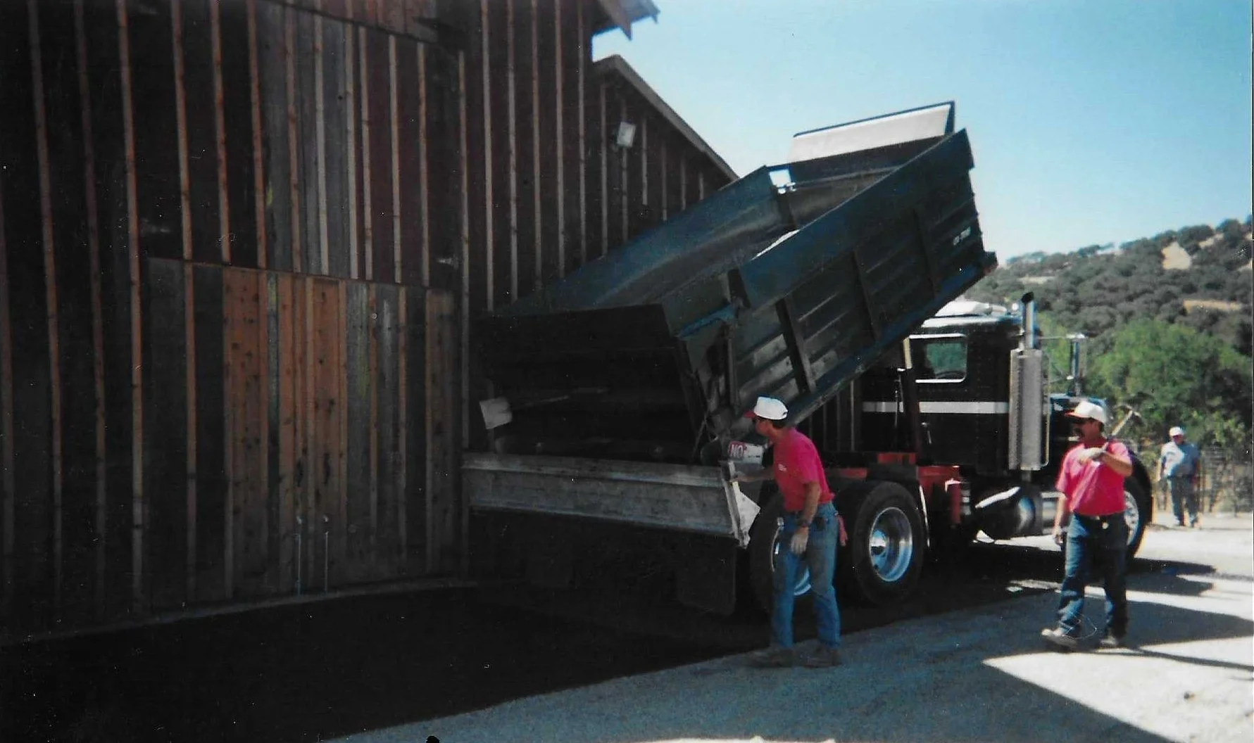 Construction workers loading a dump truck with wooden planks on a sunny day.