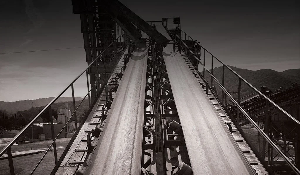 Black and white image of roller coaster tracks rising into the sky with mountains in the background.