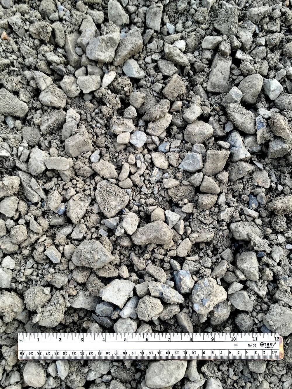 A close-up of gravel stones with a ruler at the bottom measuring several inches.
