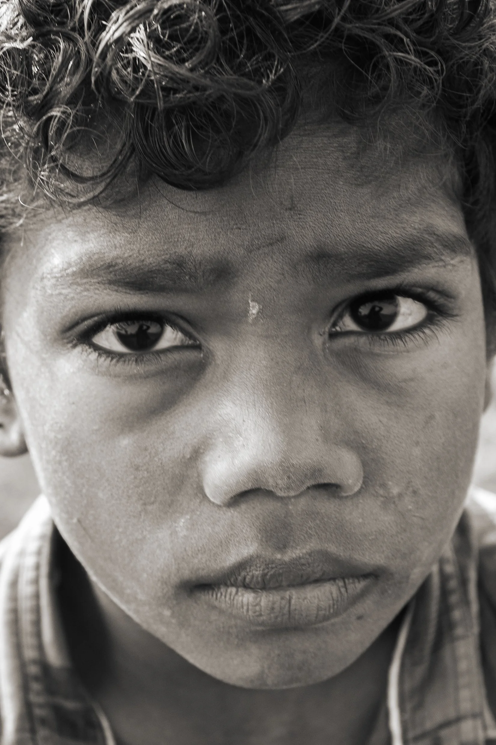 Close-up of a young child's face in black and white with curly hair, dark eyes, and youthful features.