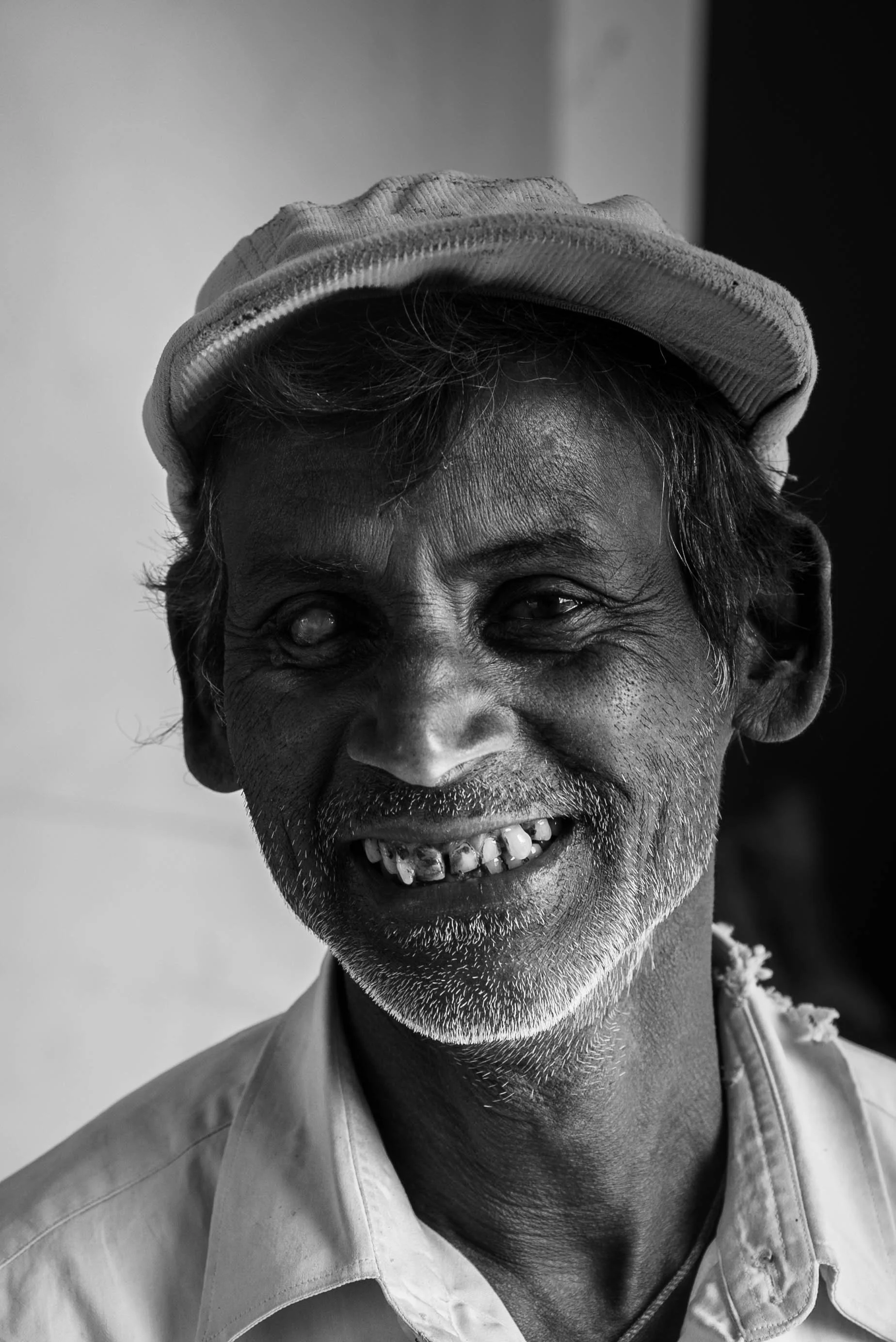Black and white photograph of an elderly man smiling, wearing a cap and a collared shirt.