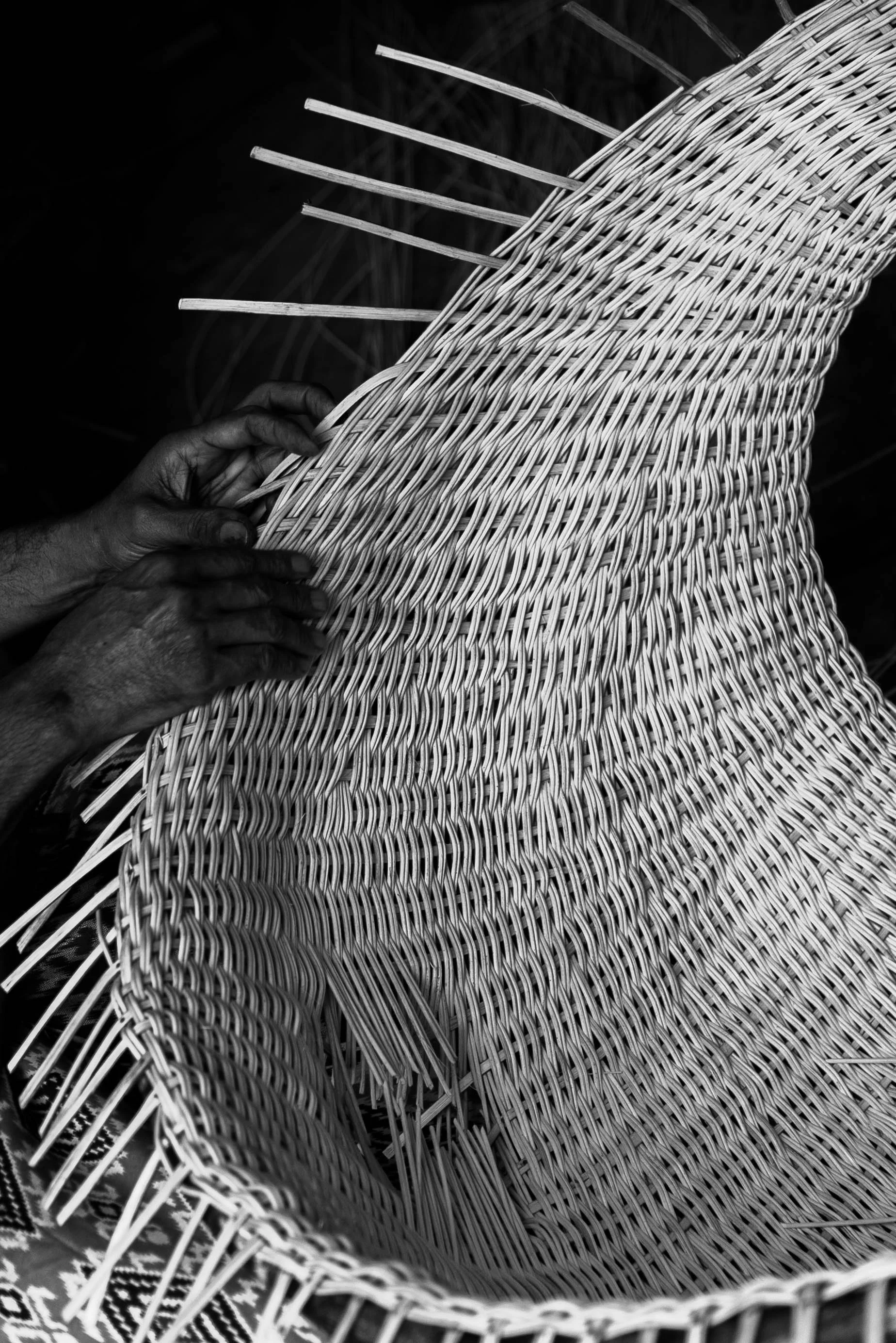 Hands weaving a wicker basket with a dark background.