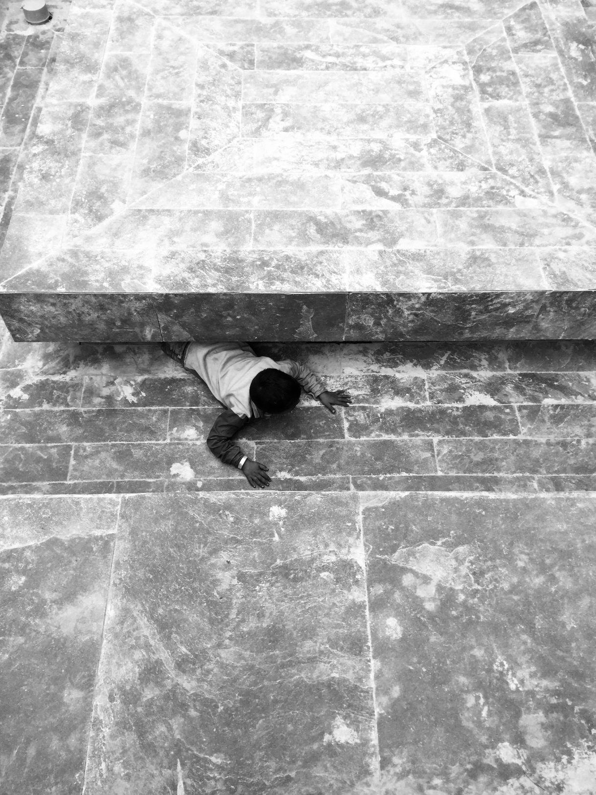 A kid crawling on a stone walkway underneath a large stone structure.