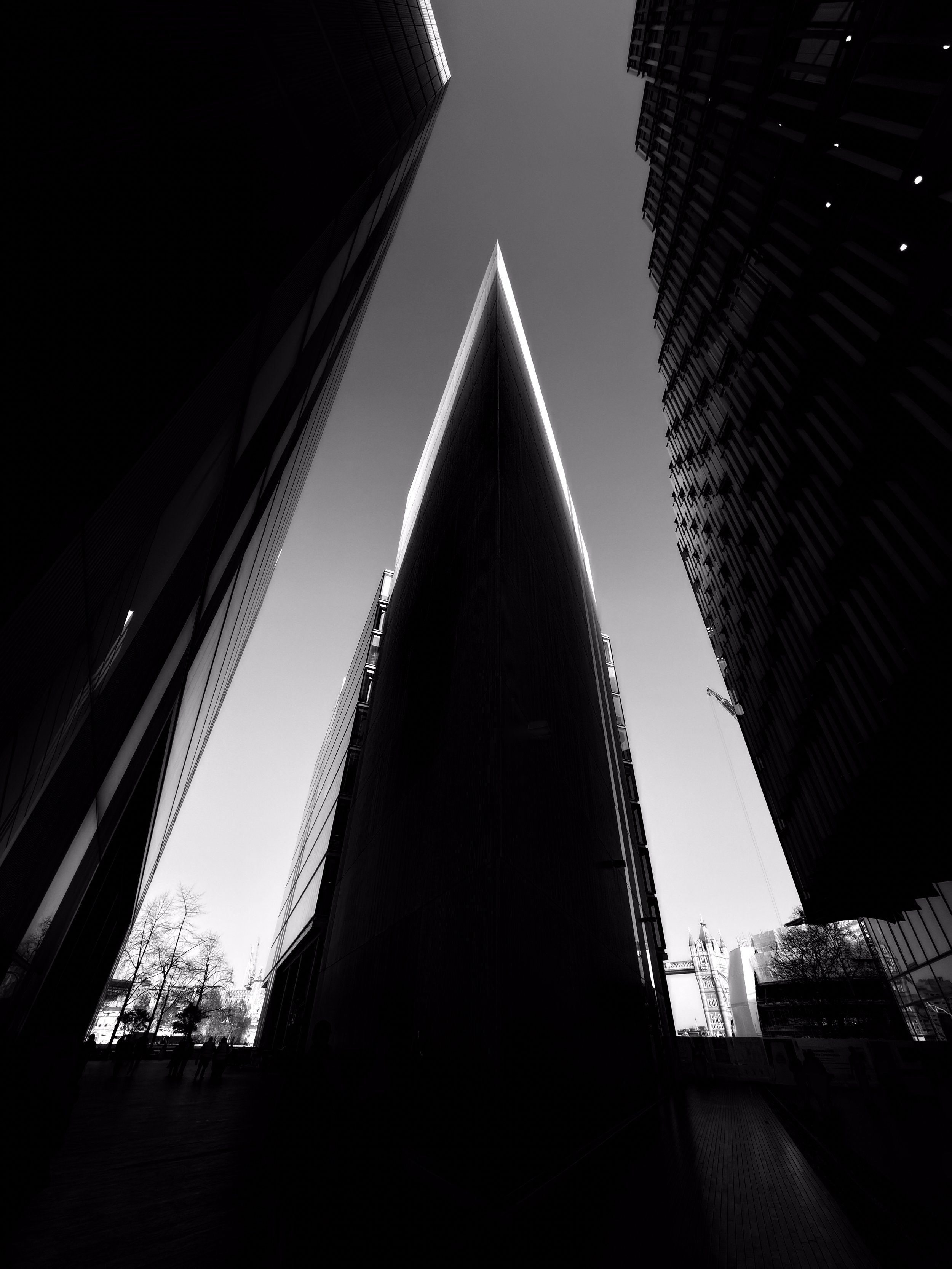Photograph of tall, modern skyscrapers taken from ground level, with sharp angles and reflective surfaces, against a clear sky.