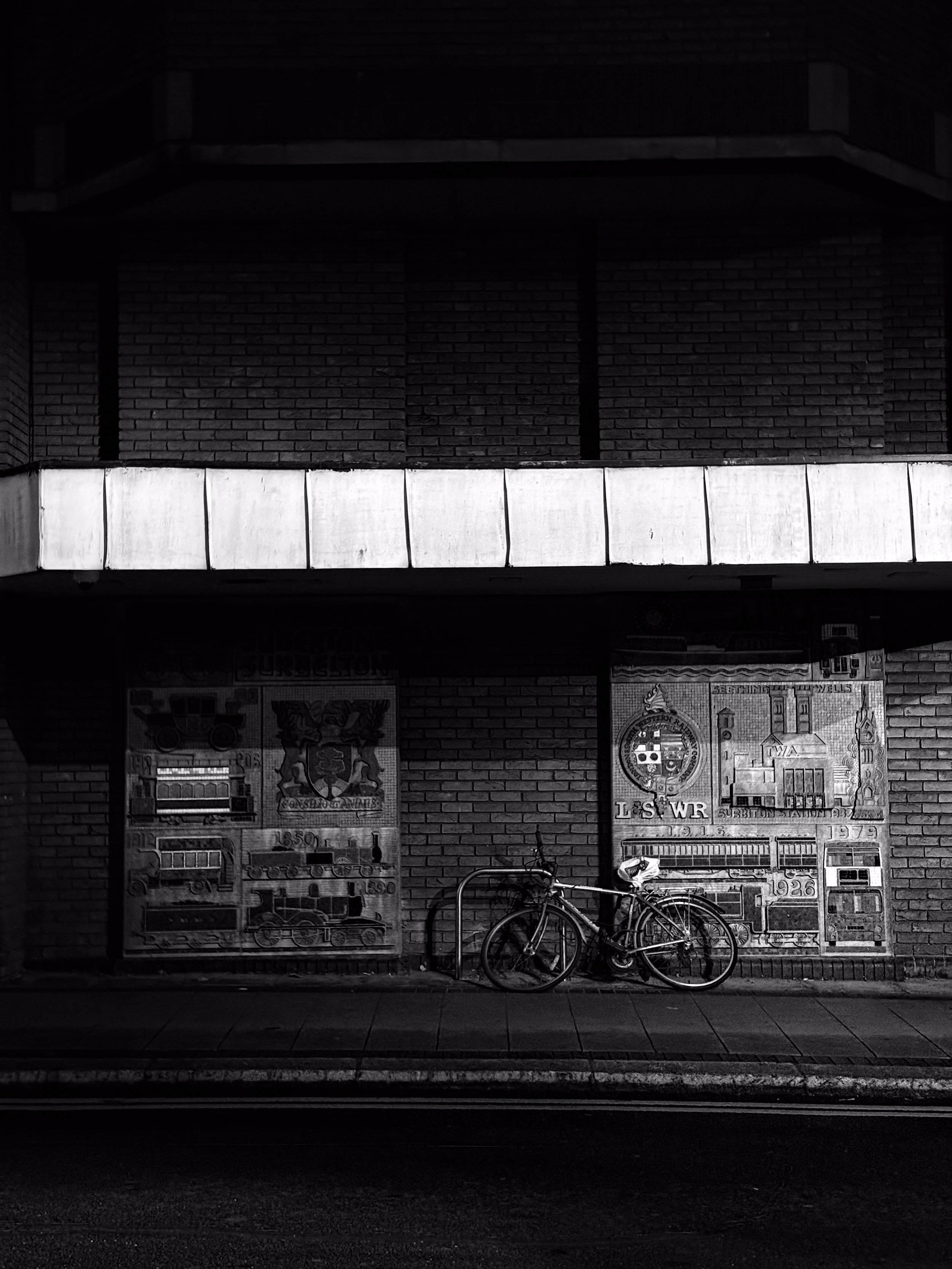 Bicycle leaning against a bike rack on a sidewalk in front of a building with brick walls and historical posters.