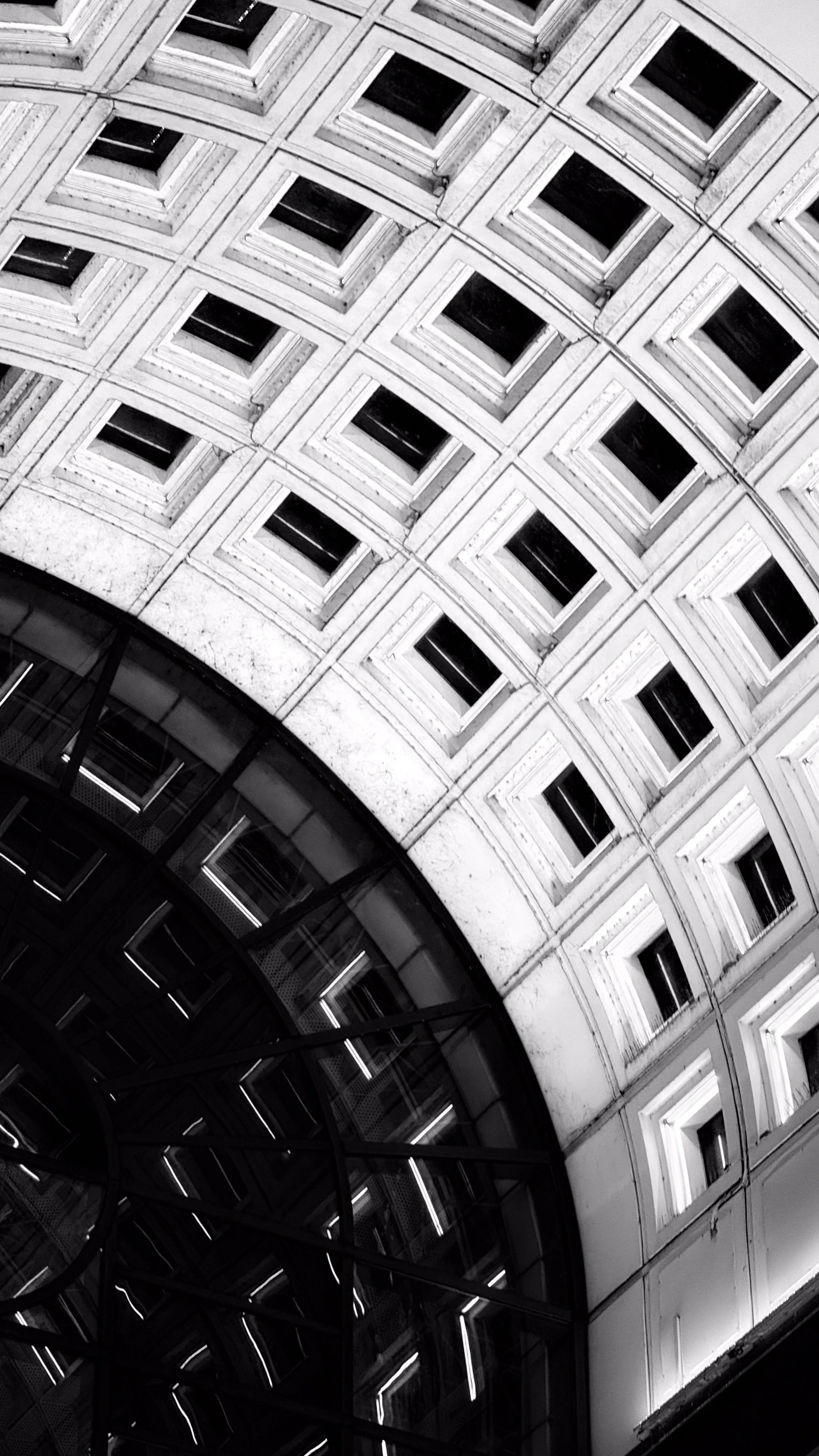 Black and white photo of a building's interior ceiling with a circular glass structure and a grid of square windows surrounding it.