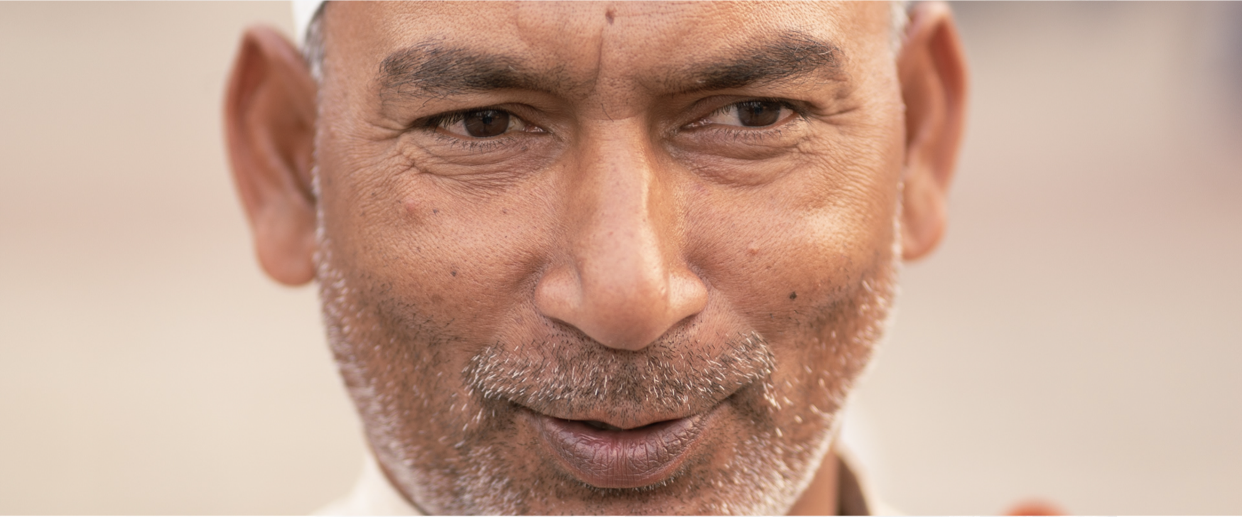 Close-up of a middle-aged man with a tan complexion, short gray hair, and a gray beard, smiling slightly.